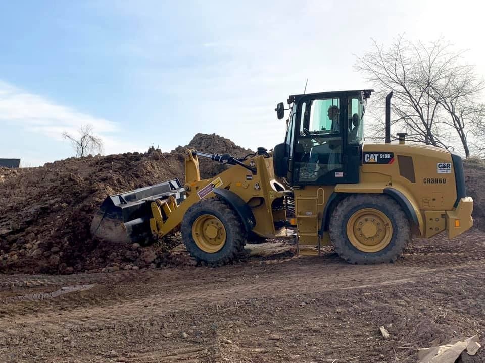 Yellow Caterpillar loader moving a large pile of dirt at an outdoor construction site.
