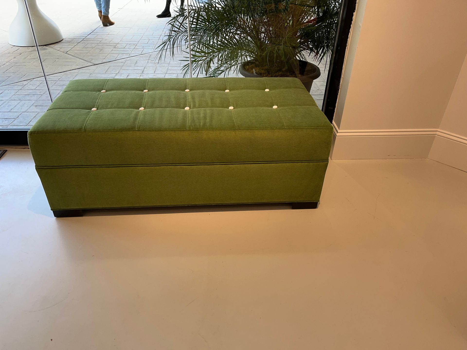 A green rectangular ottoman with button tufting sits on a light gray floor.