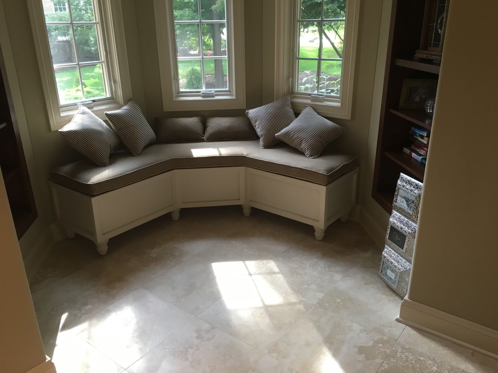 Cozy window seat with cushions and pillows in a light-filled alcove. Storage bench with white cabinets and beige upholstery.