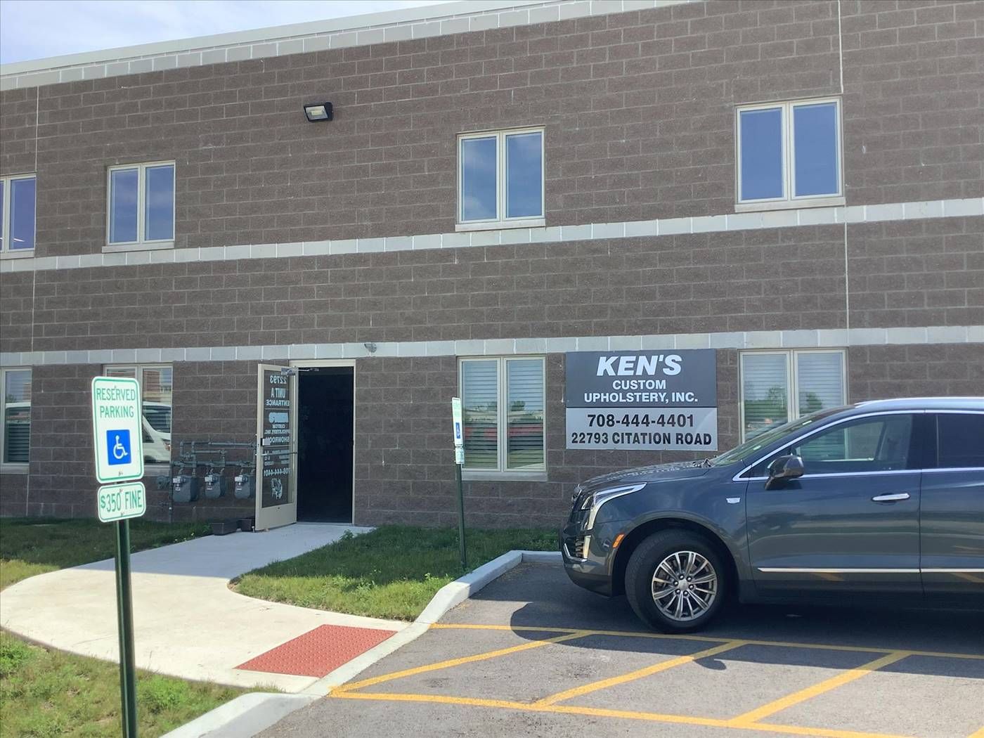 Exterior of Ken's Auto Body shop. A gray car is parked in front of the building with a handicapped parking sign visible.