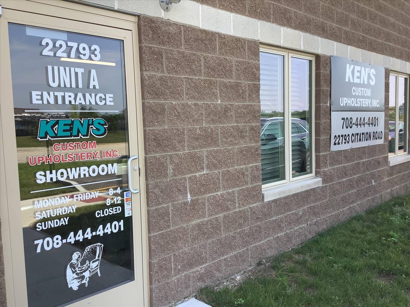 Exterior of Ken's Auto Upholstery, a business in a brick building. The entrance is marked with a door and signage.
