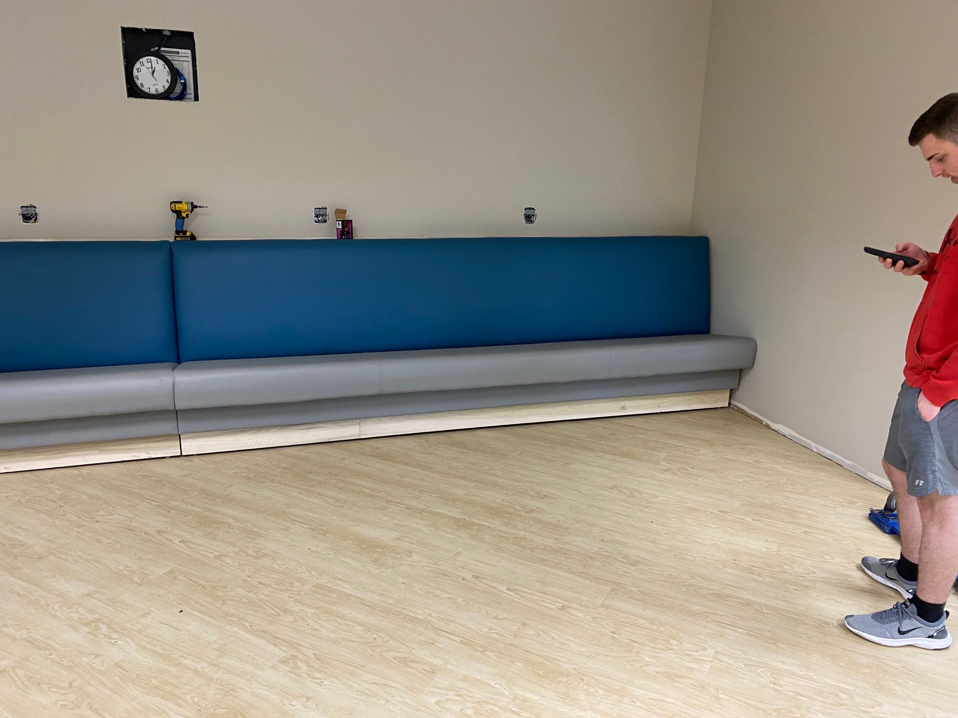Two people near a built-in blue booth with gray trim and wood-look flooring in a room under construction.