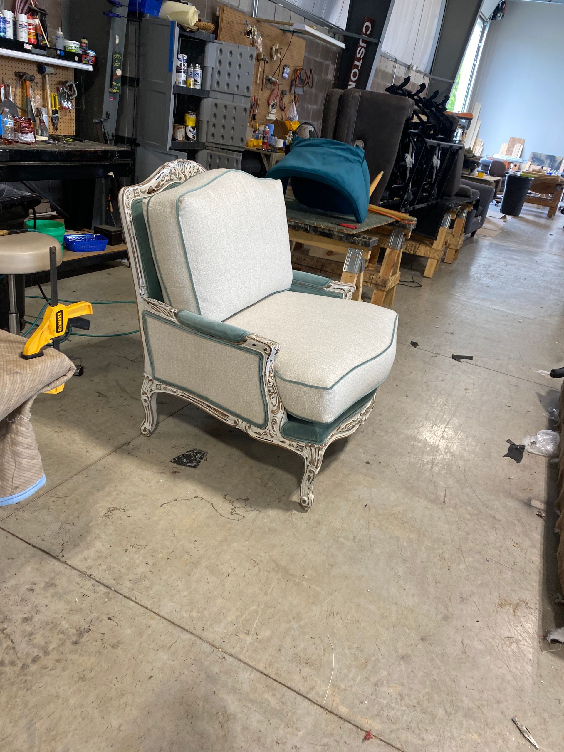 White and teal upholstered armchair in a workshop setting. The chair has a decorative frame, and the seat and back cushions are light-colored.