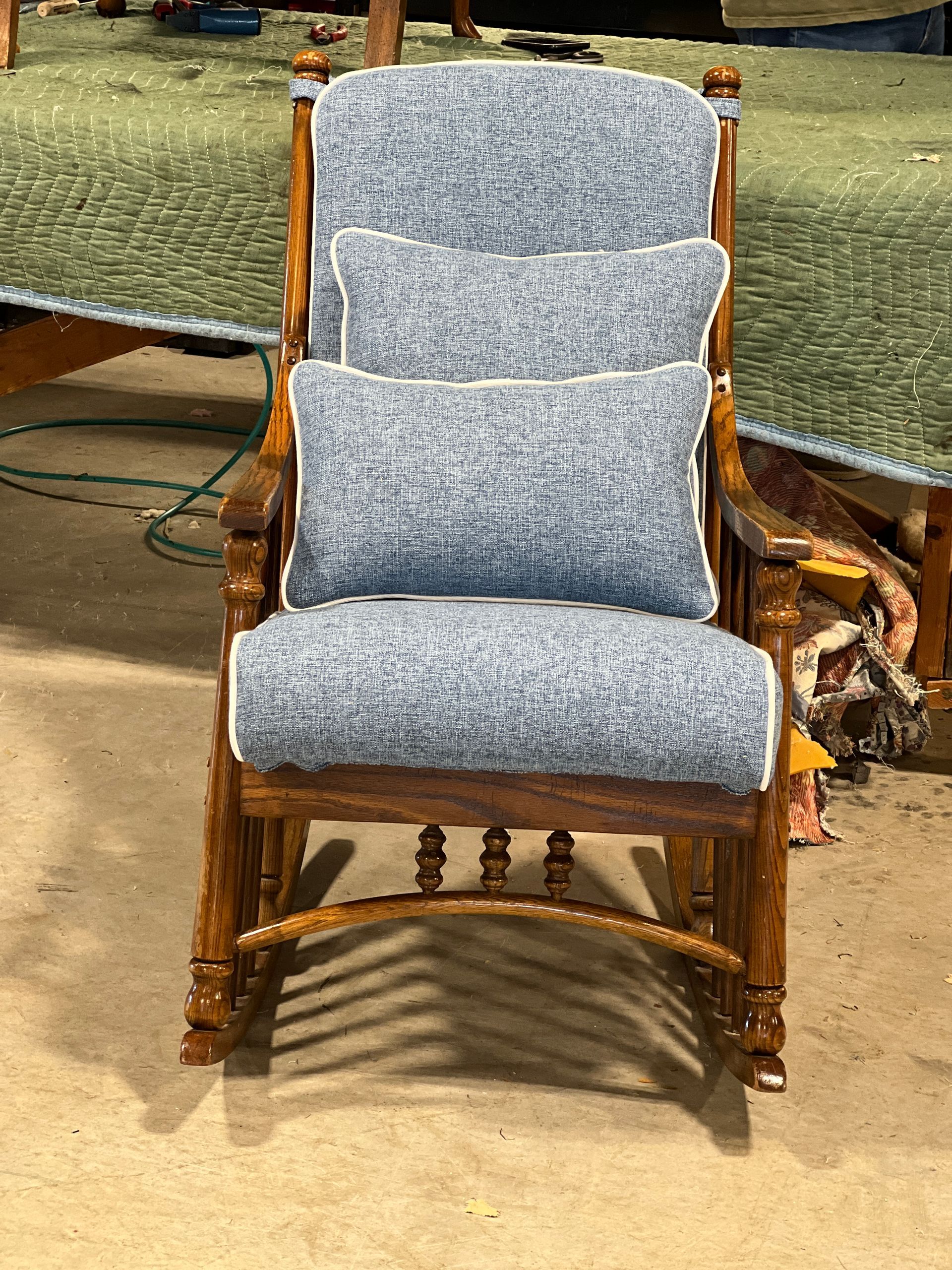 A wooden rocking chair with blue cushions and white trim, set against a blurred background.
