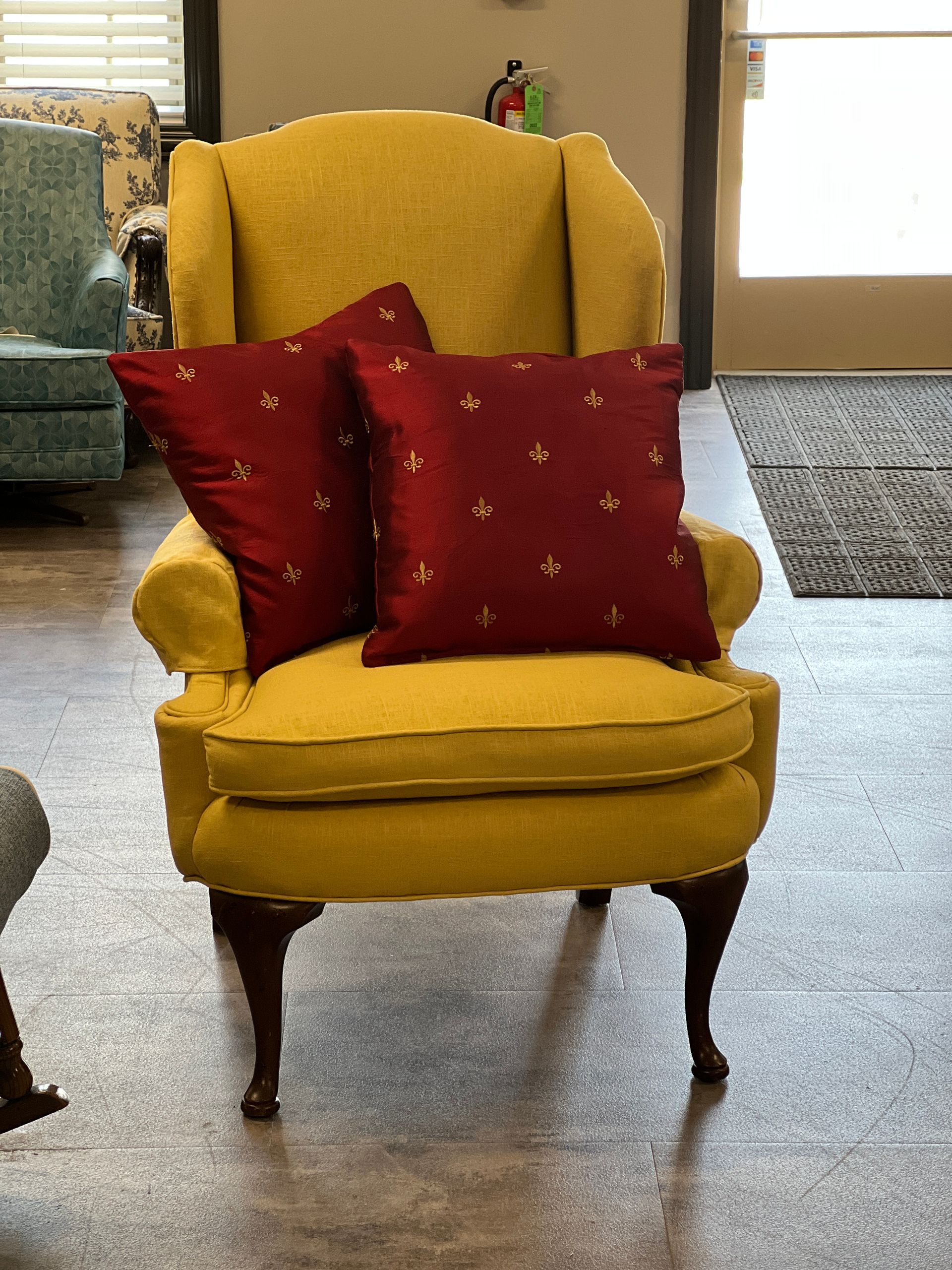Yellow armchair with two red decorative pillows. The chair sits on wood floors.