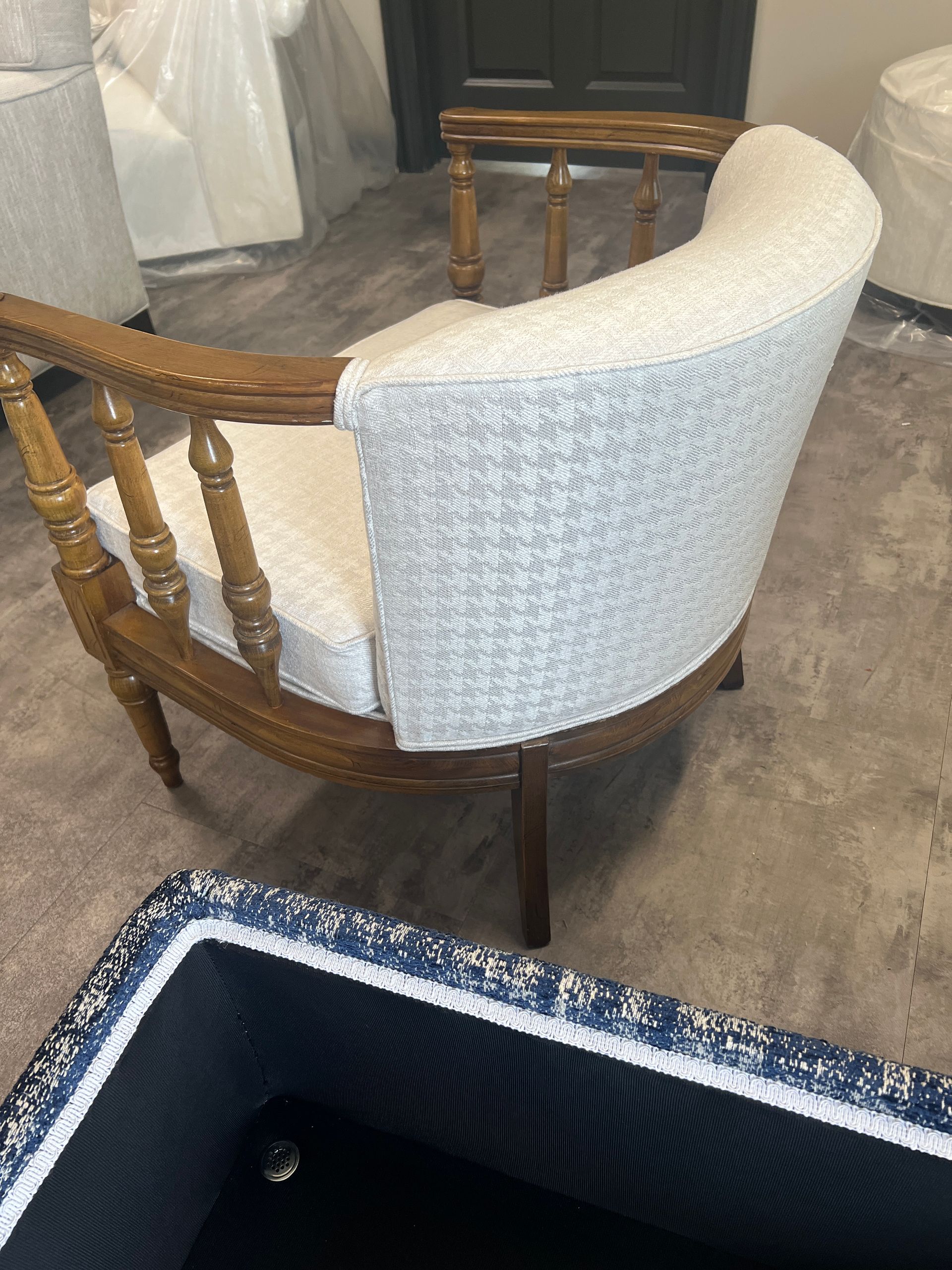 Wooden captain's chair with light-colored patterned upholstery. It's in a room with other furniture, including a partial view of a navy blue item.