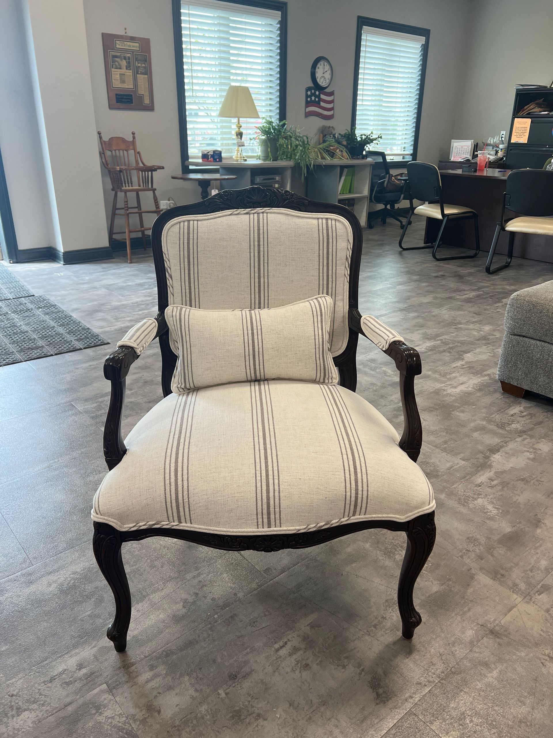 Antique-style armchair with a light fabric, striped pattern, and small pillow. Dark wooden frame, indoors.