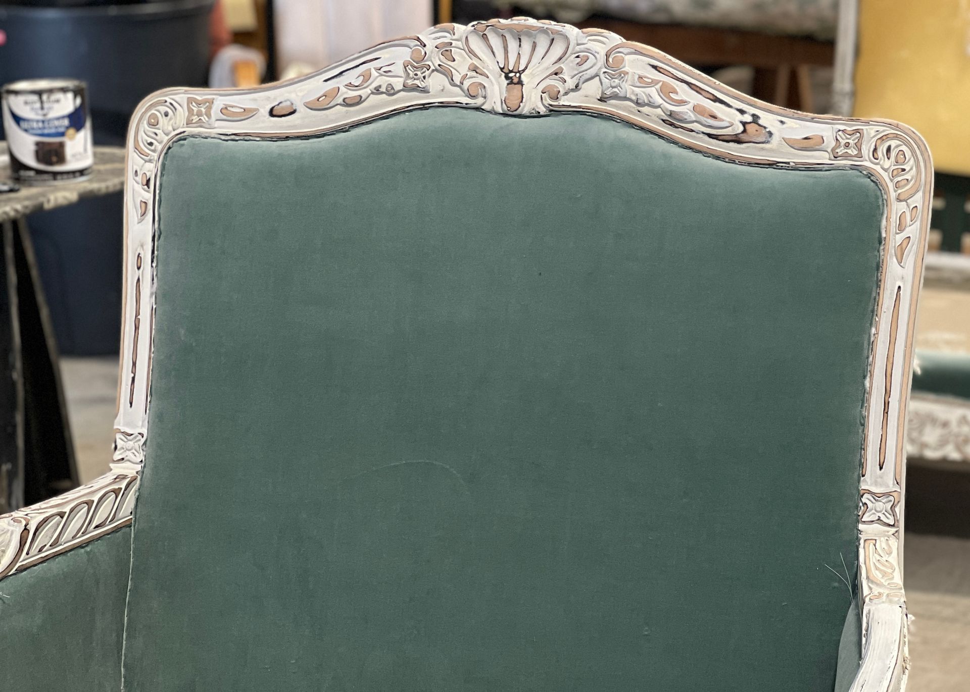 Close-up of a velvet chair back in teal, framed by a white, ornate carved wooden border.
