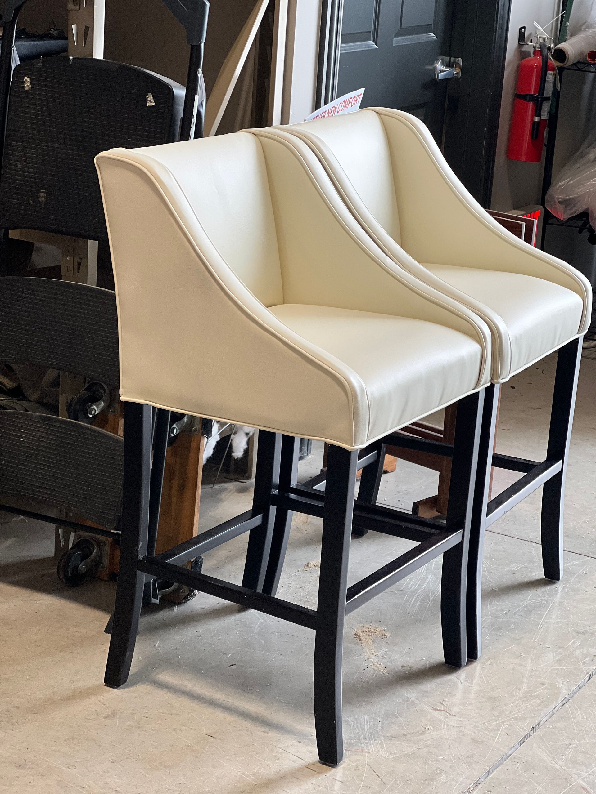 Two cream-colored bar stools with black legs, side by side. They have curved backs and are set indoors.