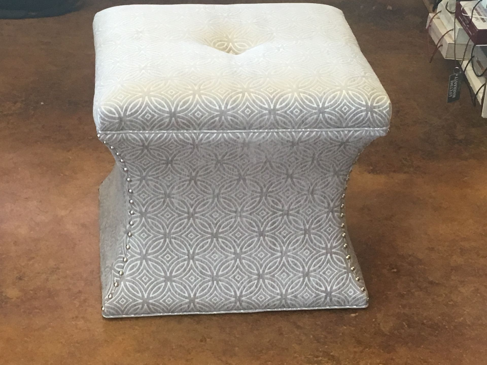 Upholstered ottoman with geometric pattern and buttoned top, set against a brown floor.