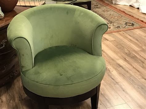 A close-up of a dusty green swivel chair with a dark wooden base and armrests, in a room with wood flooring and a rug.