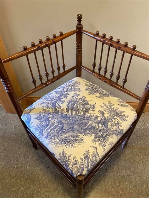 A wooden corner chair with a blue and white toile-covered seat. The chair has a decorative back with spindles and finials.