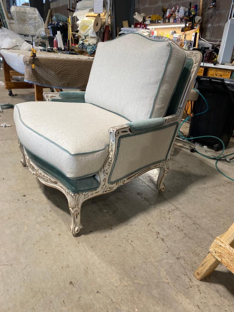 Upholstered armchair with white fabric, teal trim, and ornate white wooden frame in a workshop.