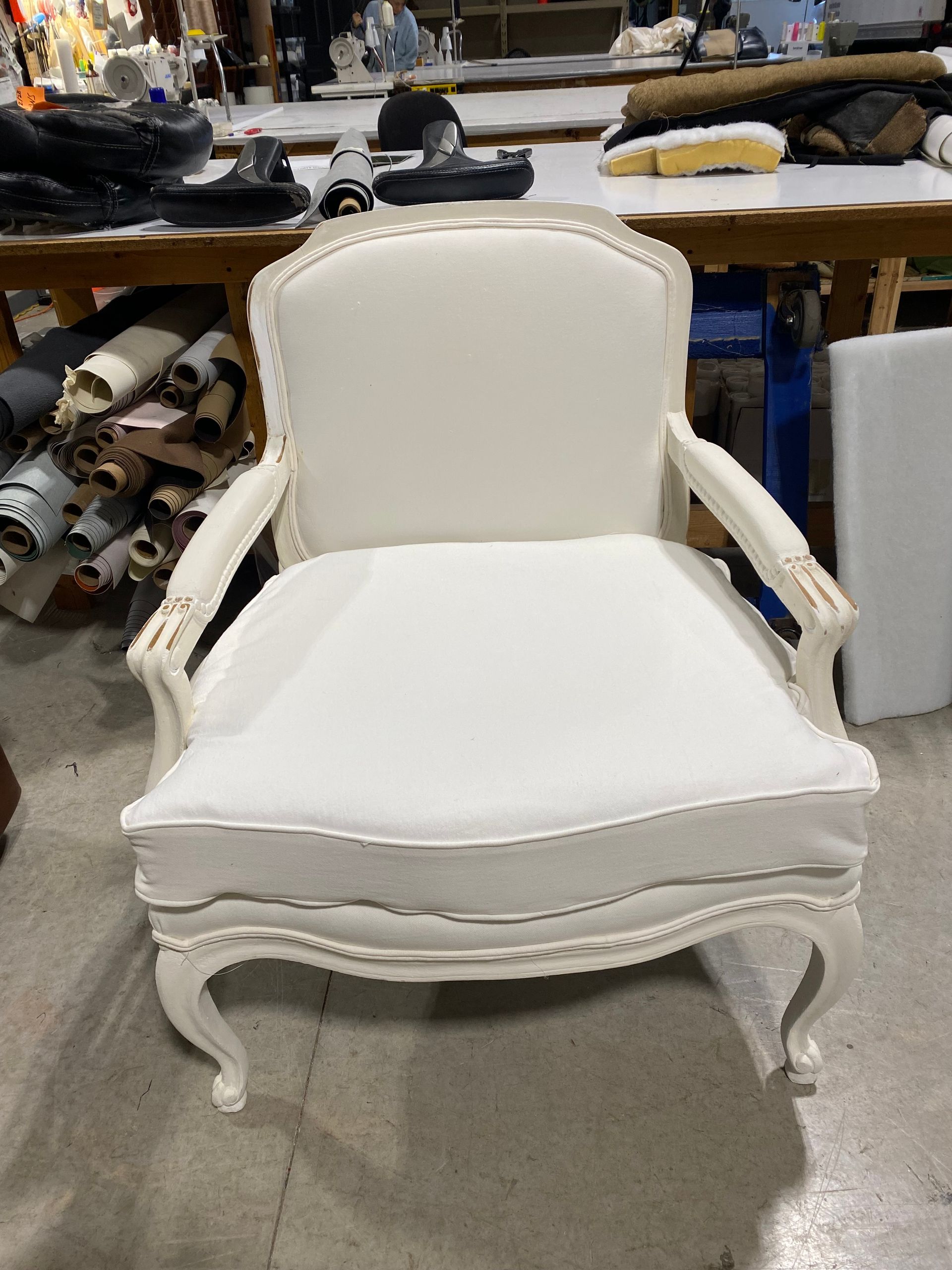 White upholstered armchair with ornate wooden frame in a workshop setting.