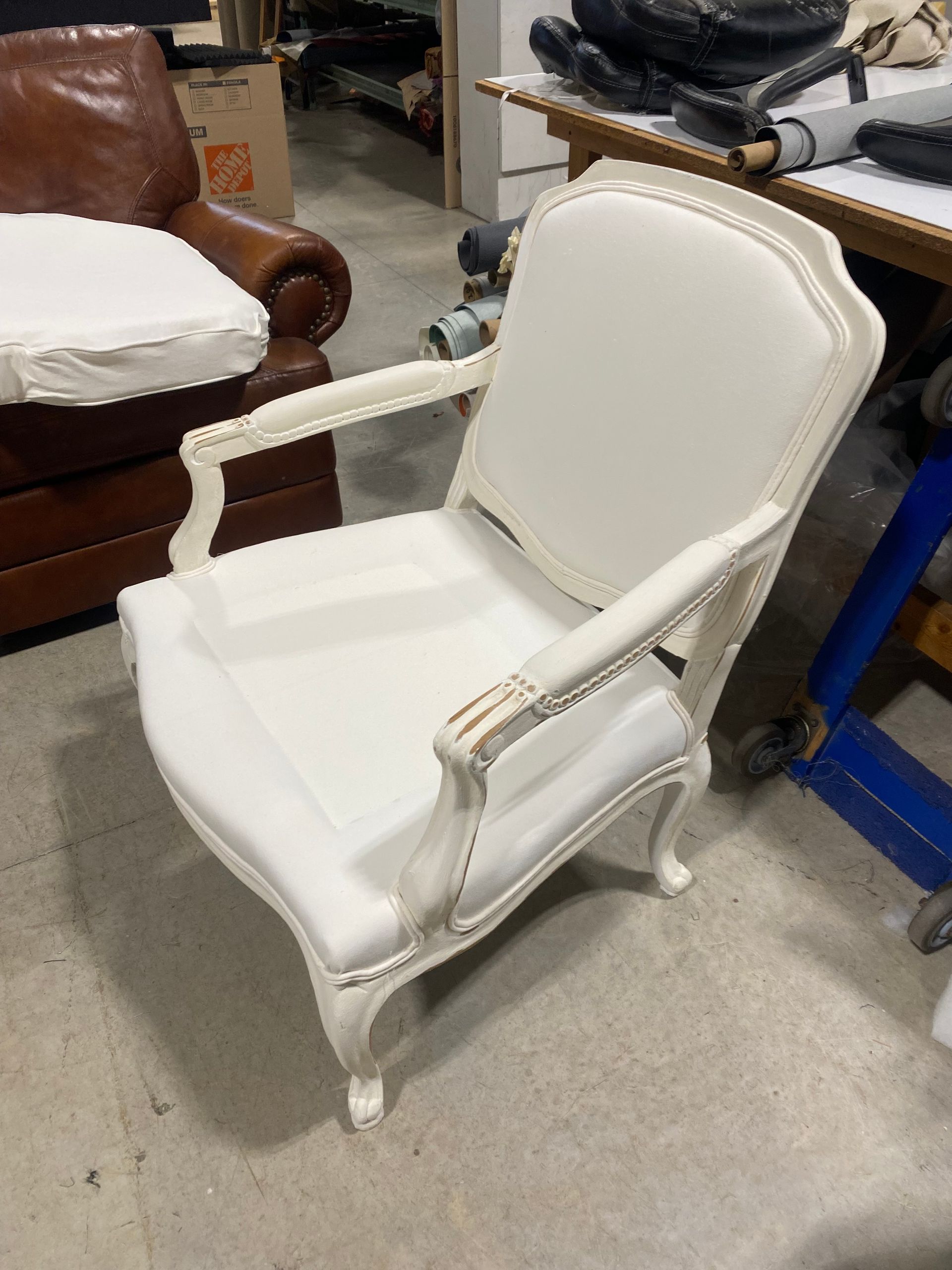 White upholstered antique chair with decorative trim, in a workshop setting.