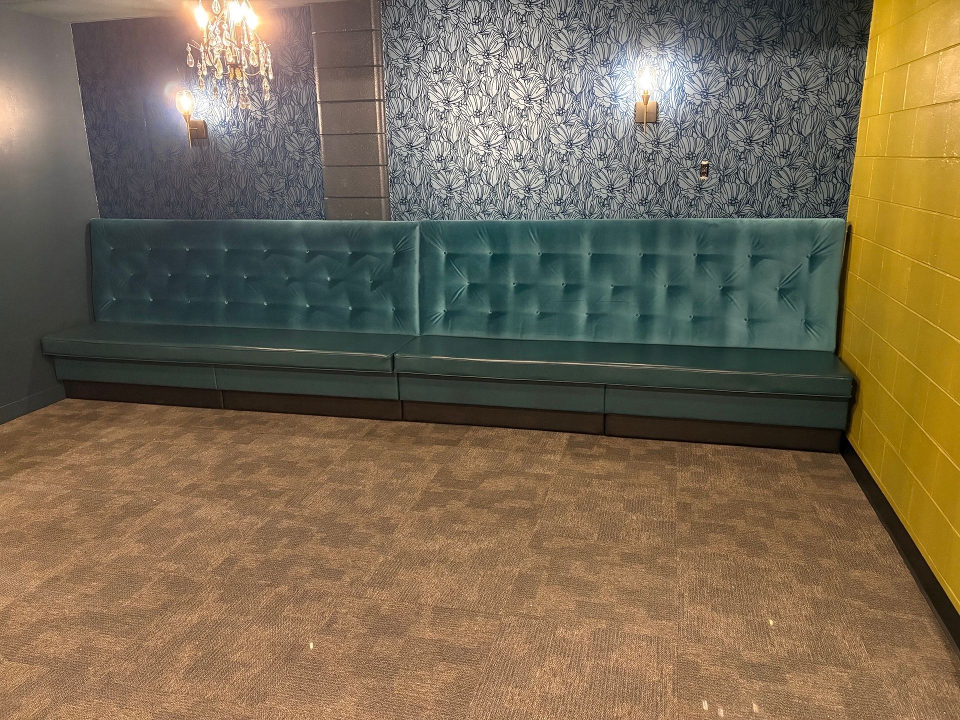 Long turquoise bench against a patterned wall, with lights and a yellow wall, on a carpeted floor.