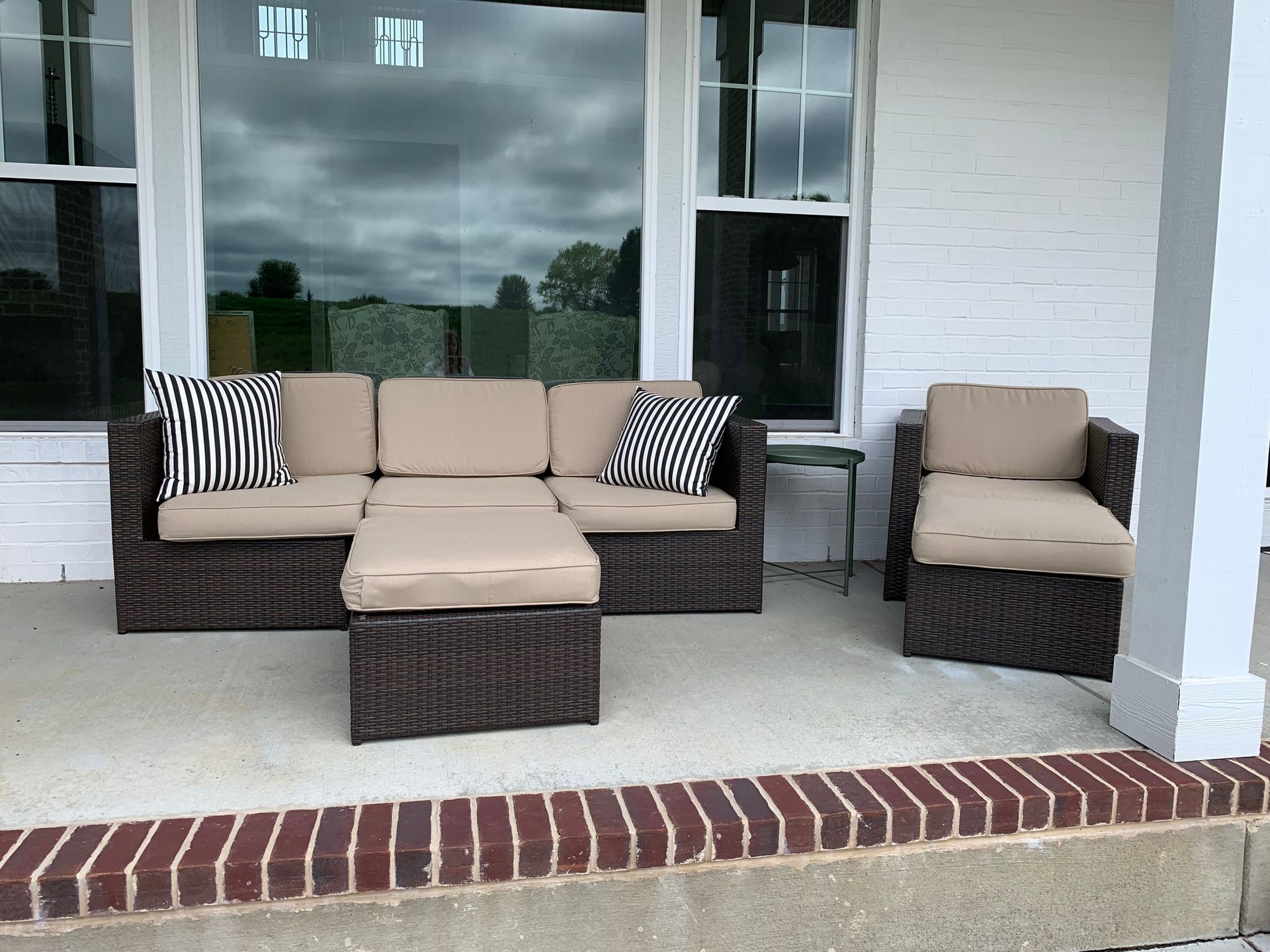 Outdoor wicker furniture set on a porch: sofa, ottoman, chair, and side table.