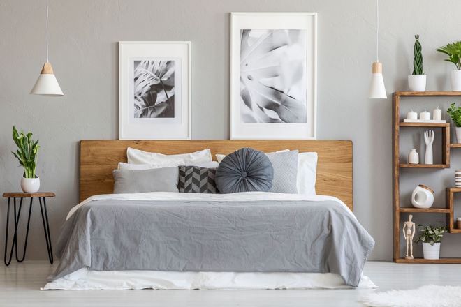 Bedroom with a bed, wooden headboard, gray bedding, decorative pillows, framed art, side table, and a wooden shelf with plants.
