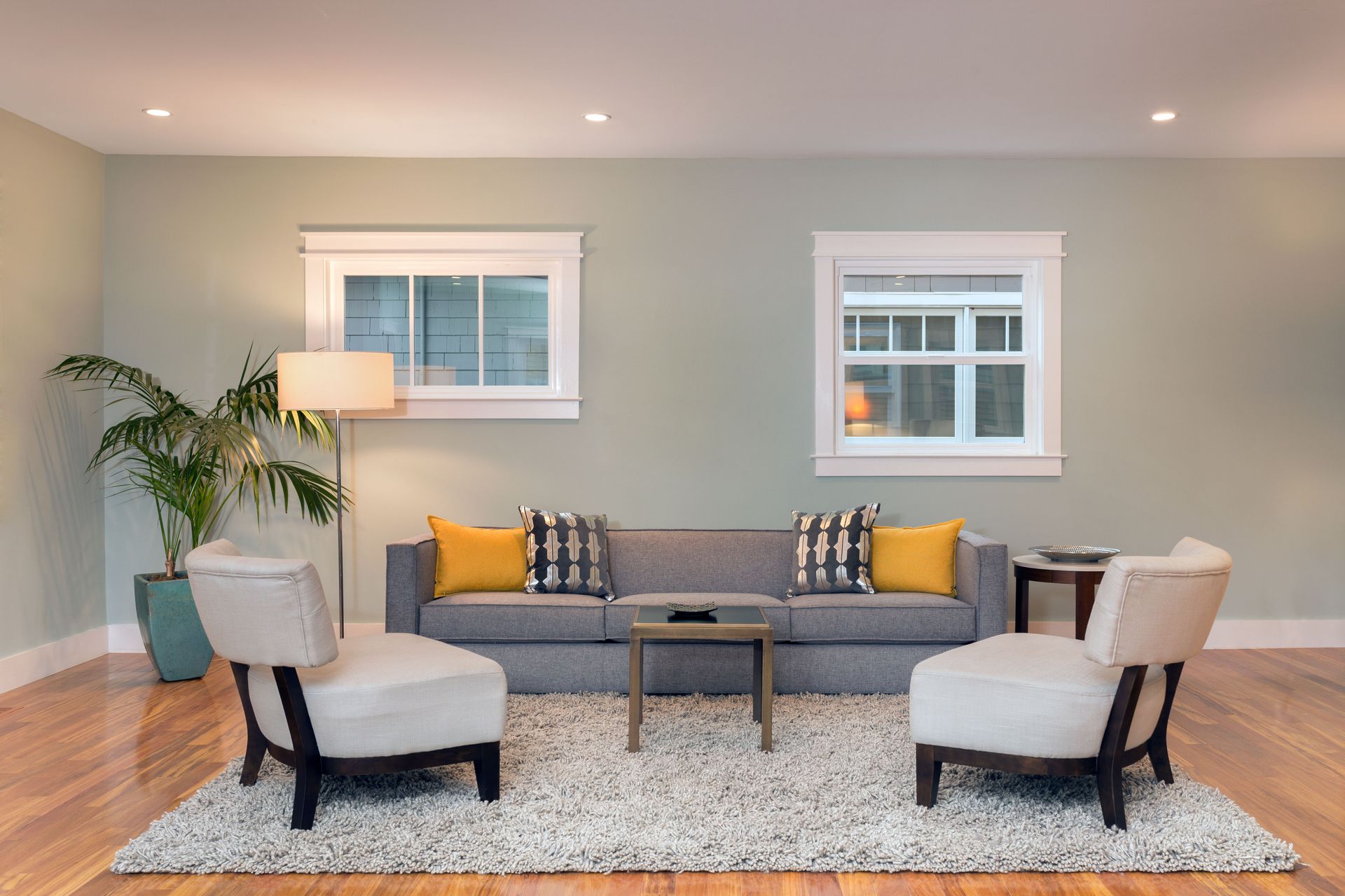 Living room with gray sofa, two white armchairs, and rug, with light green walls, and wooden floor.