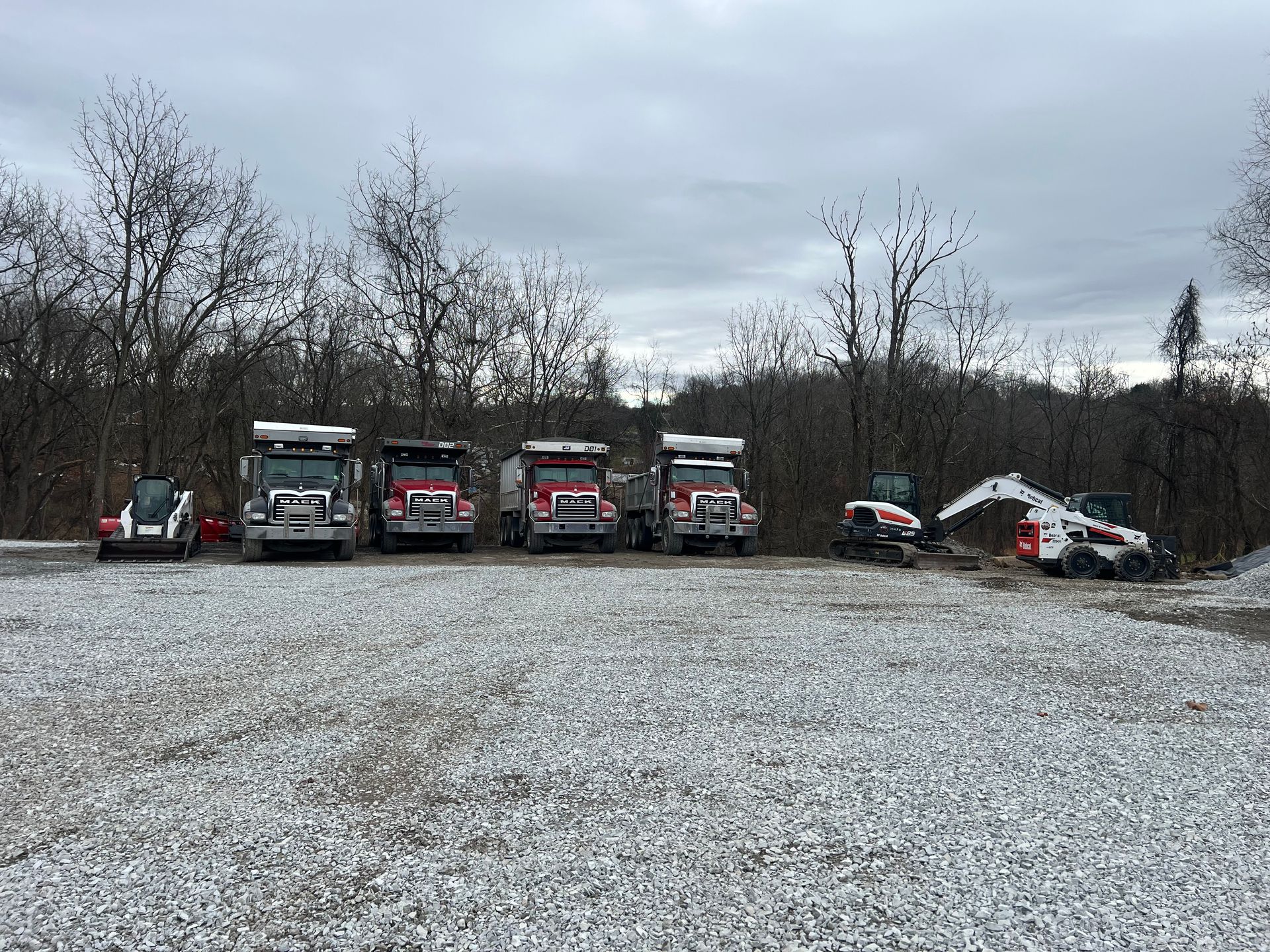 A row of dump trucks are parked in a gravel lot.