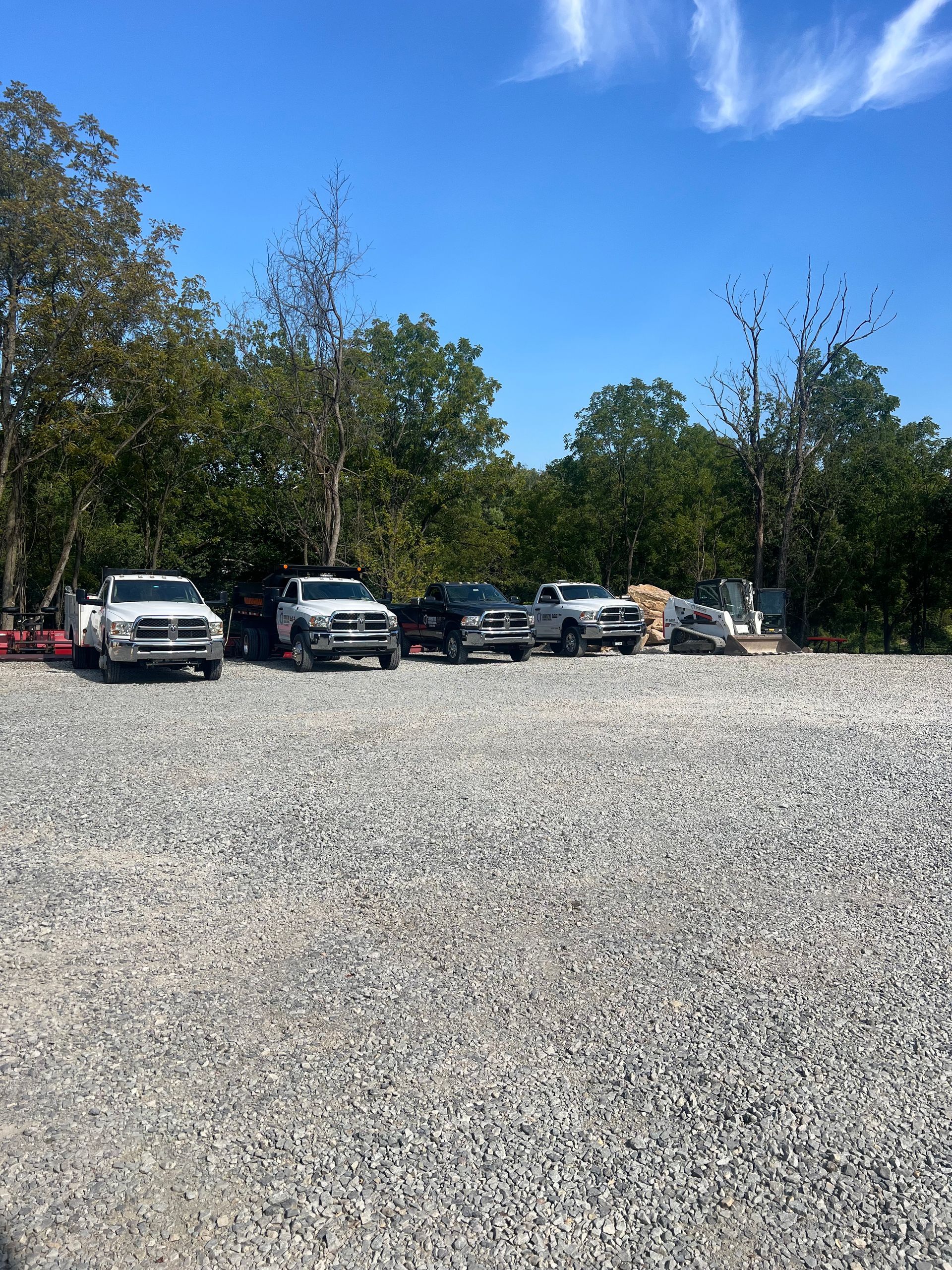A row of trucks are parked in a gravel lot.