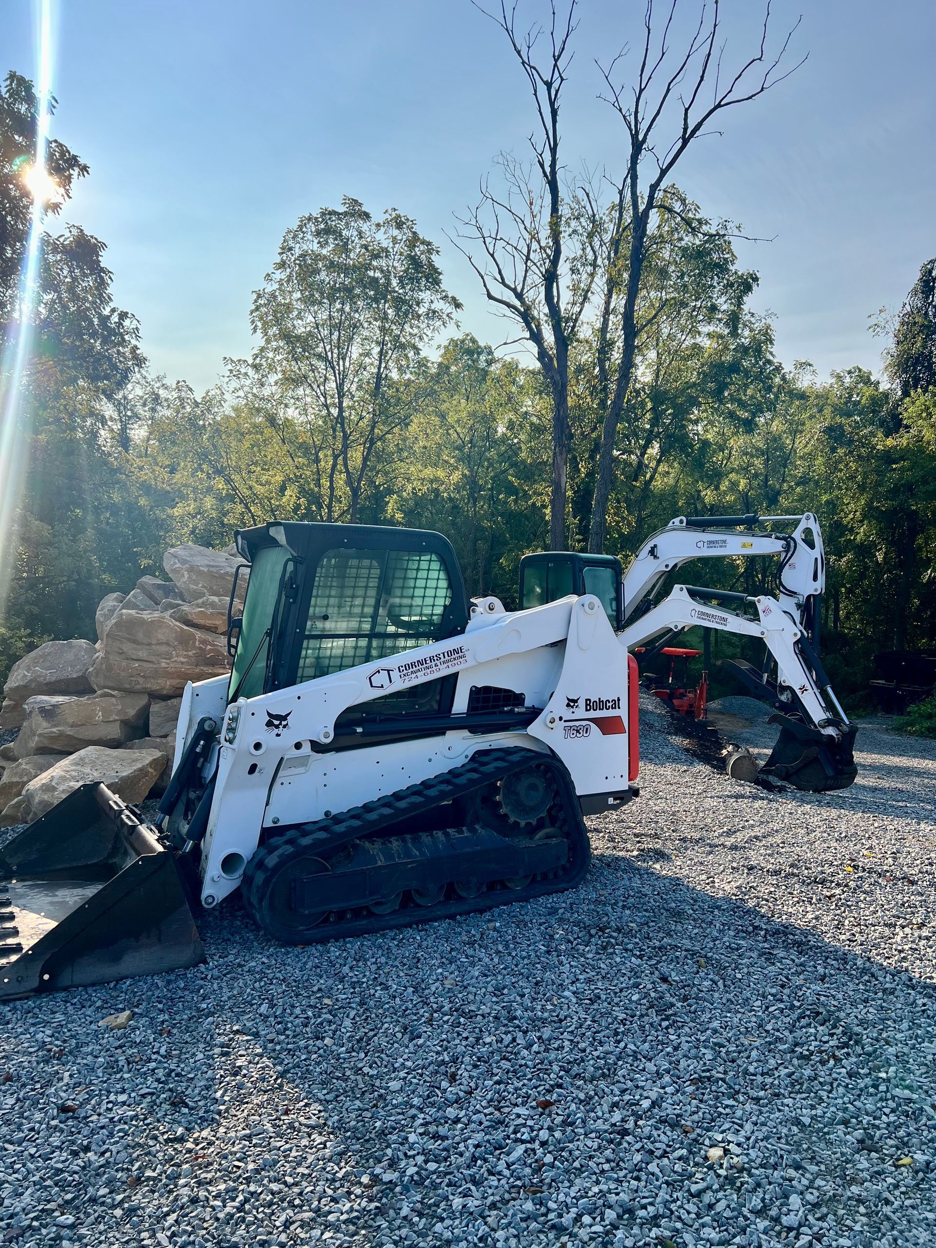 A bobcat is parked on a gravel road next to a pile of rocks.
