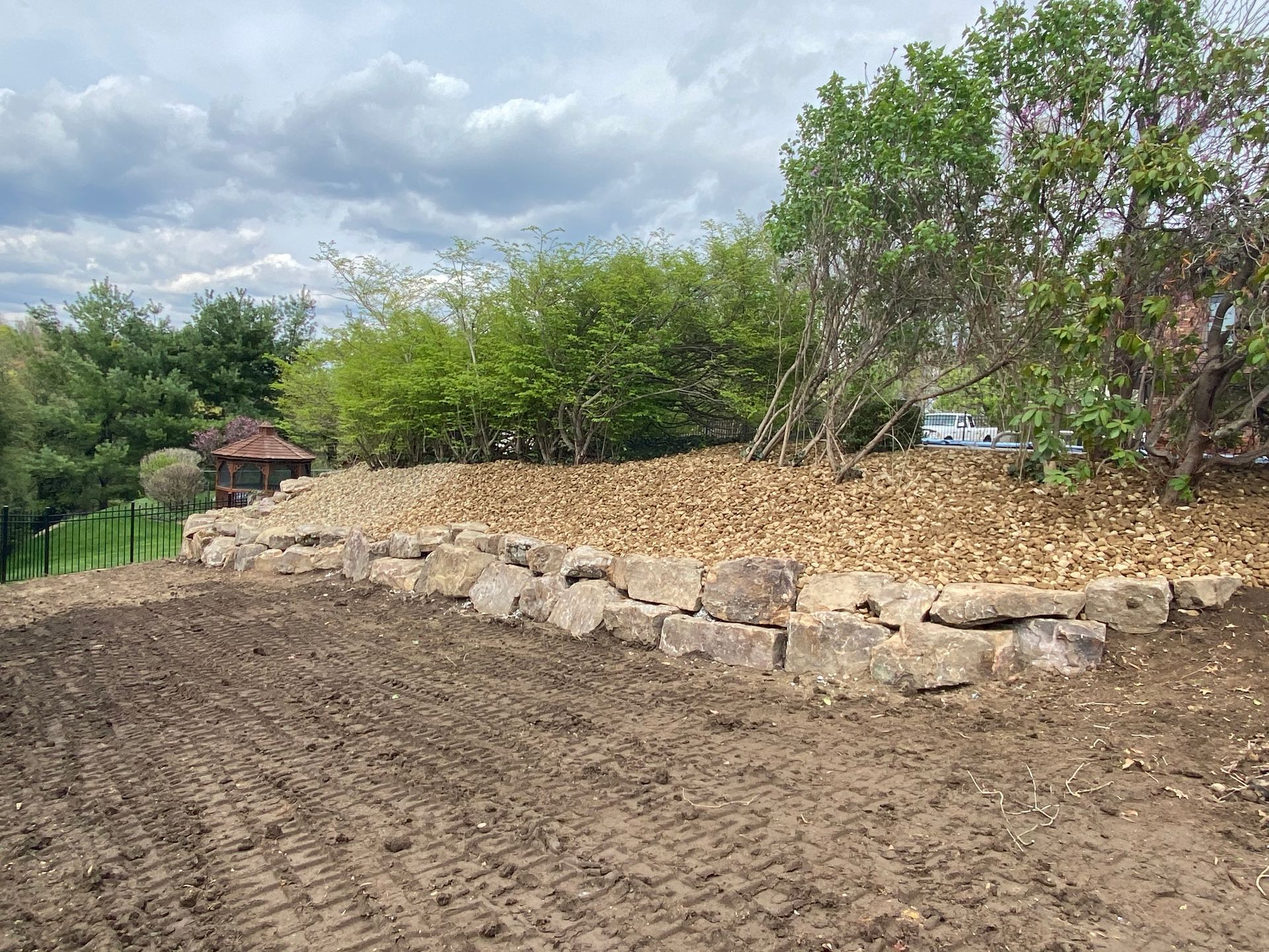 A dirt field with a stone wall and trees in the background.