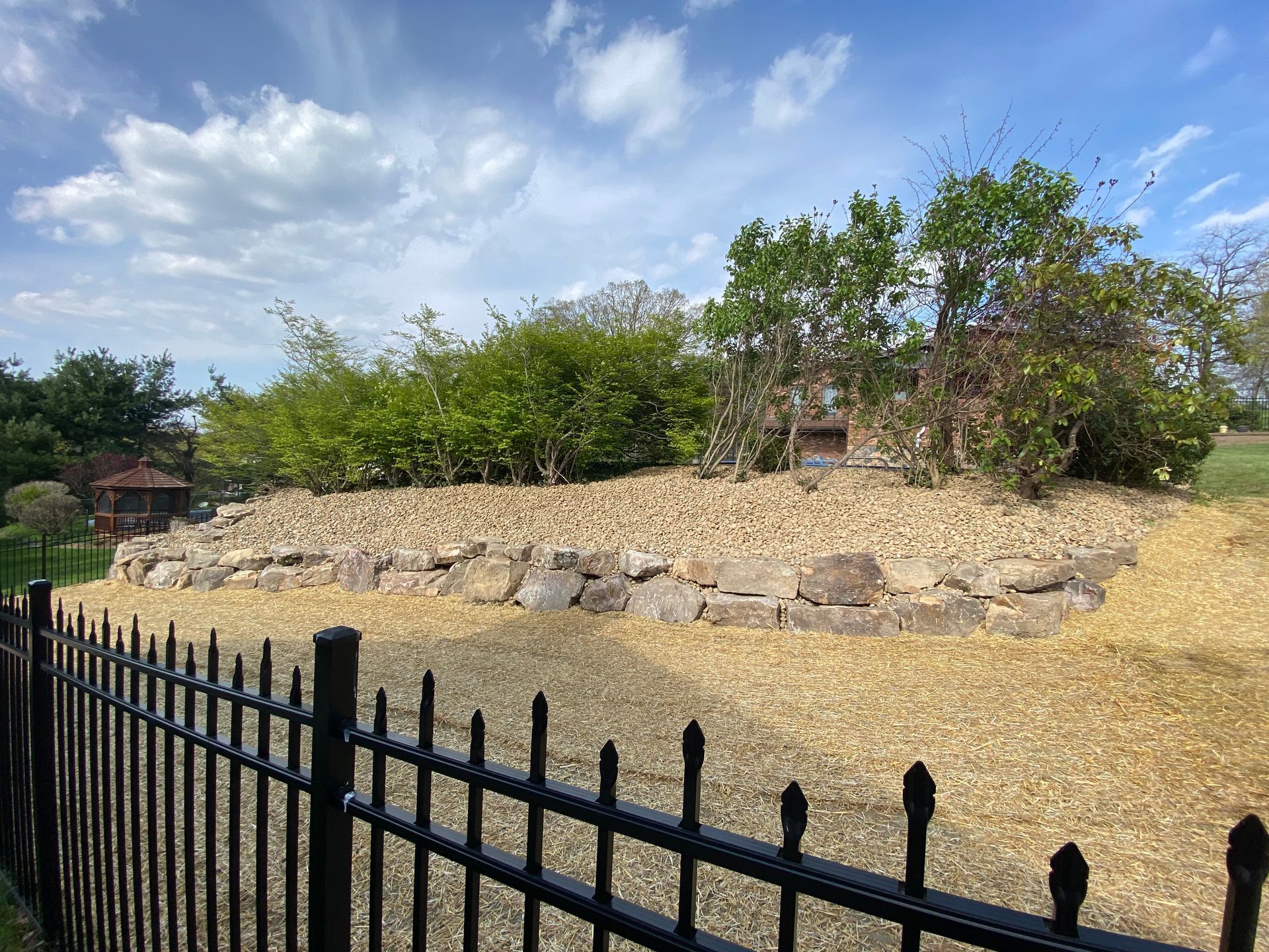 A black fence surrounds a rocky area with trees in the background.