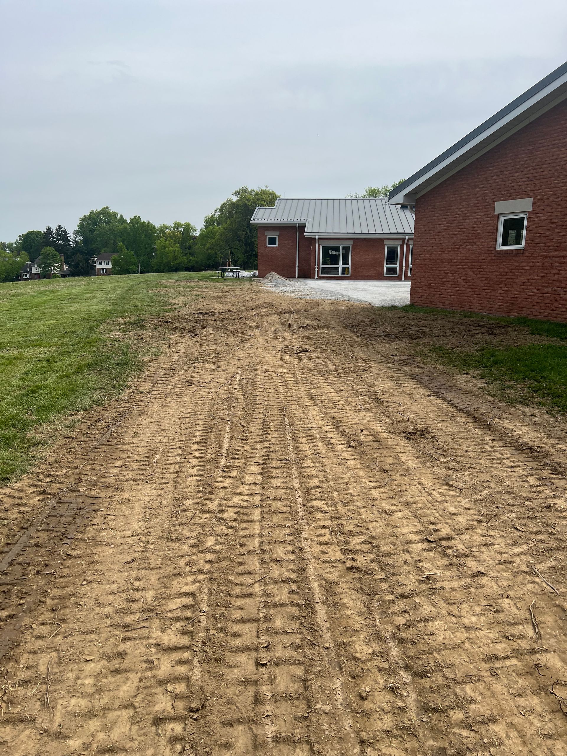 A dirt road leading to a brick house in a field.