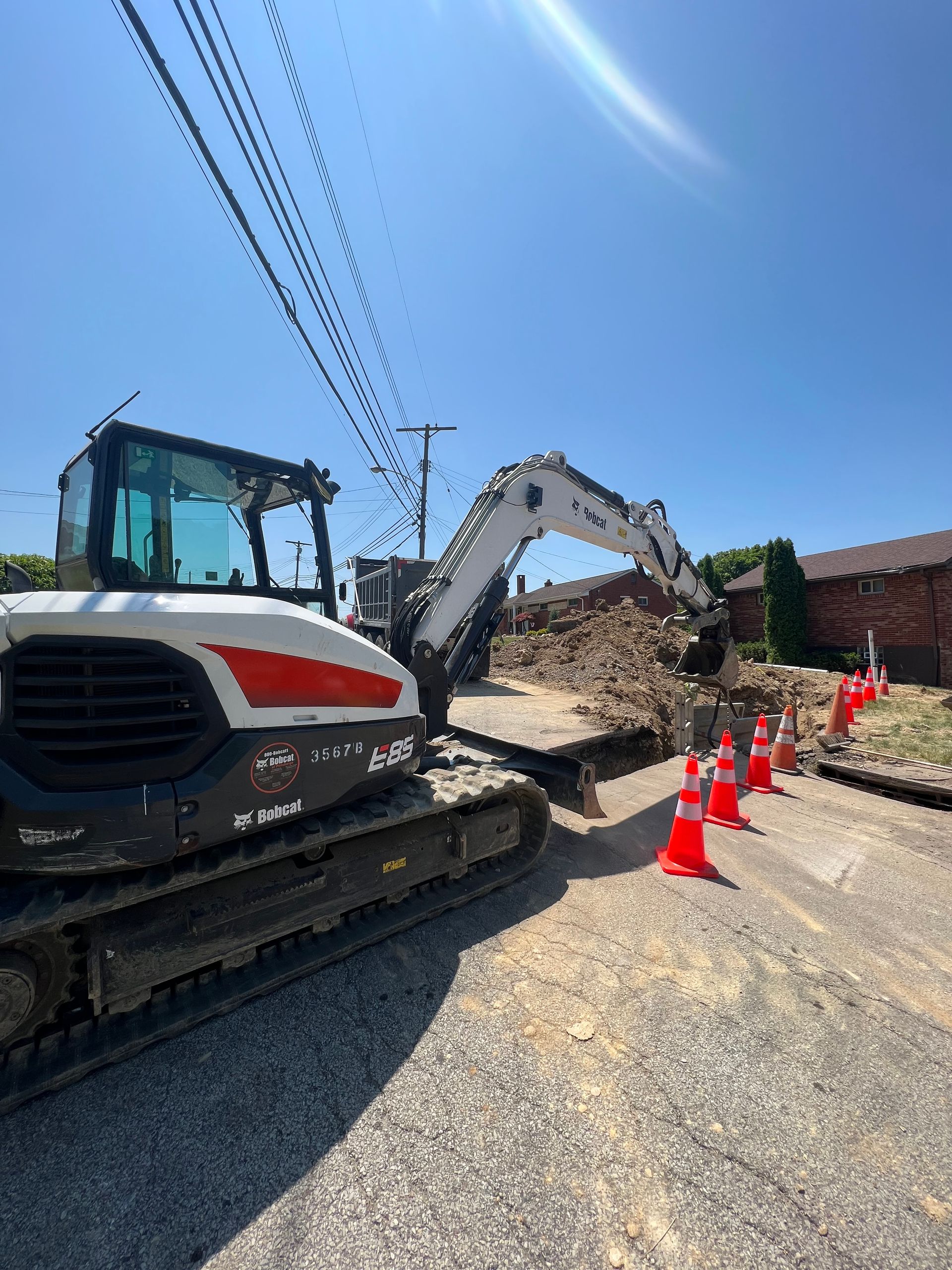 A bulldozer is parked on the side of the road next to a row of orange cones.