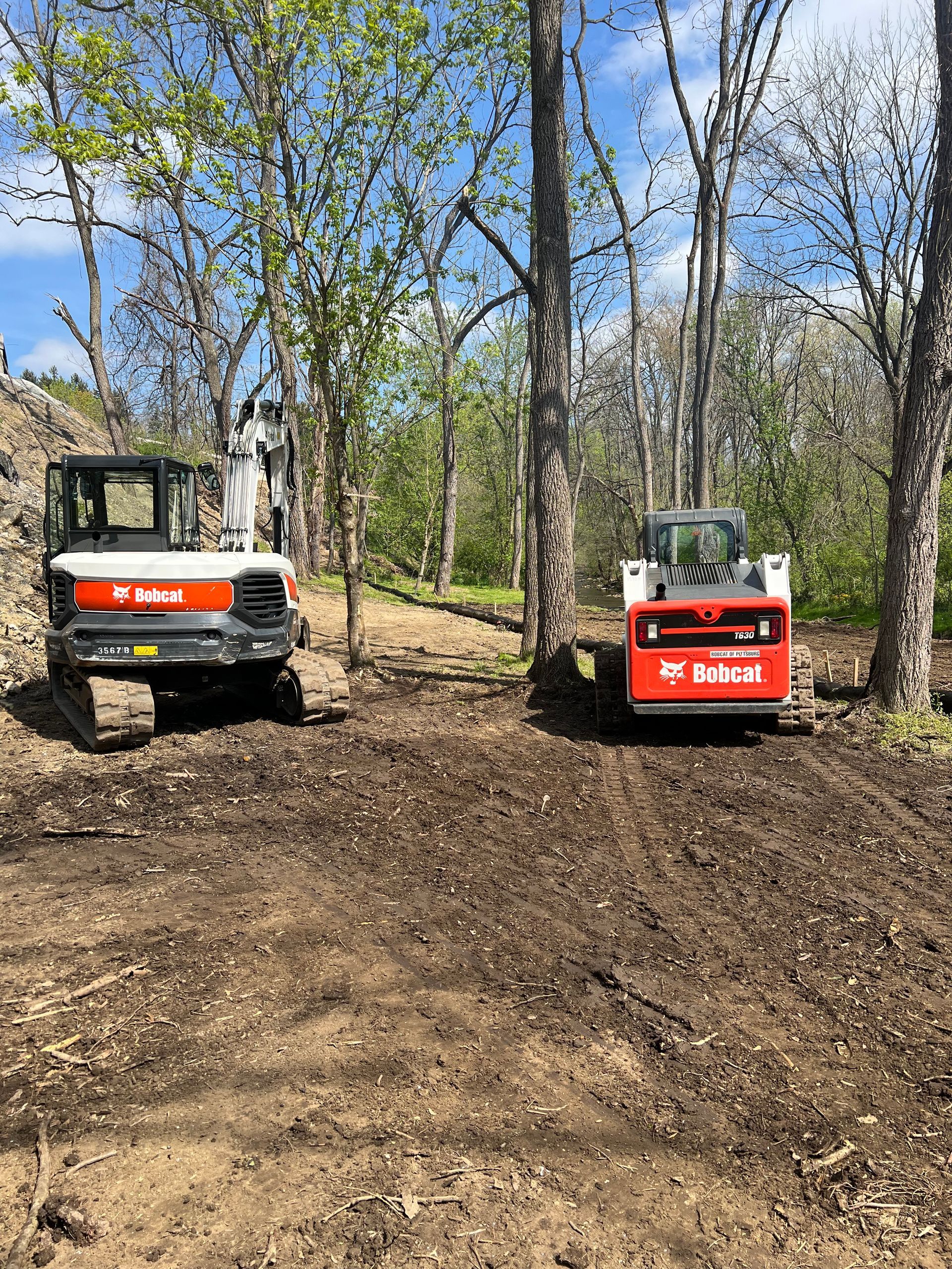 Two bobcat tractors are parked next to each other in a dirt field.