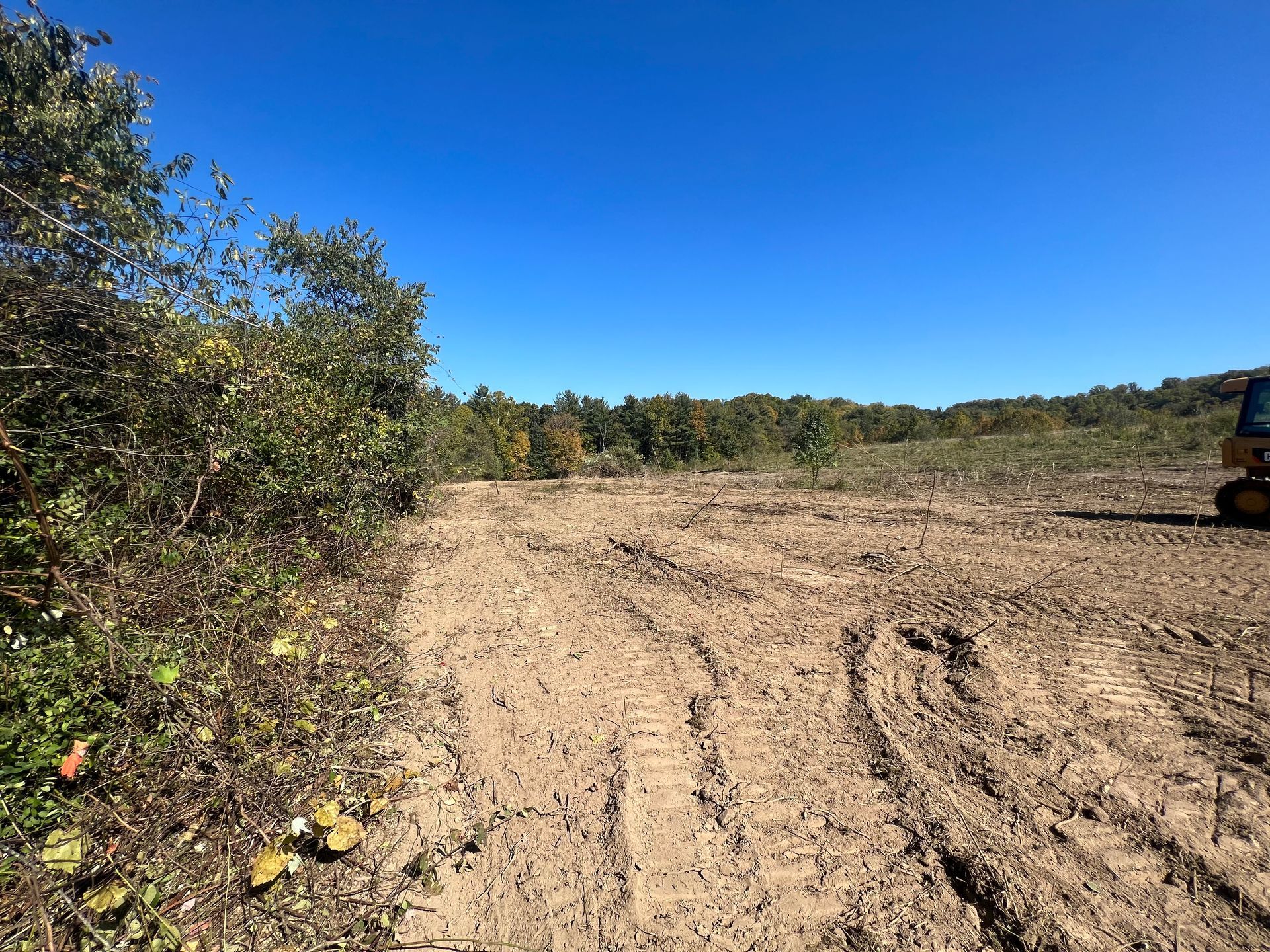 A bulldozer is driving through a dirt field with trees in the background.