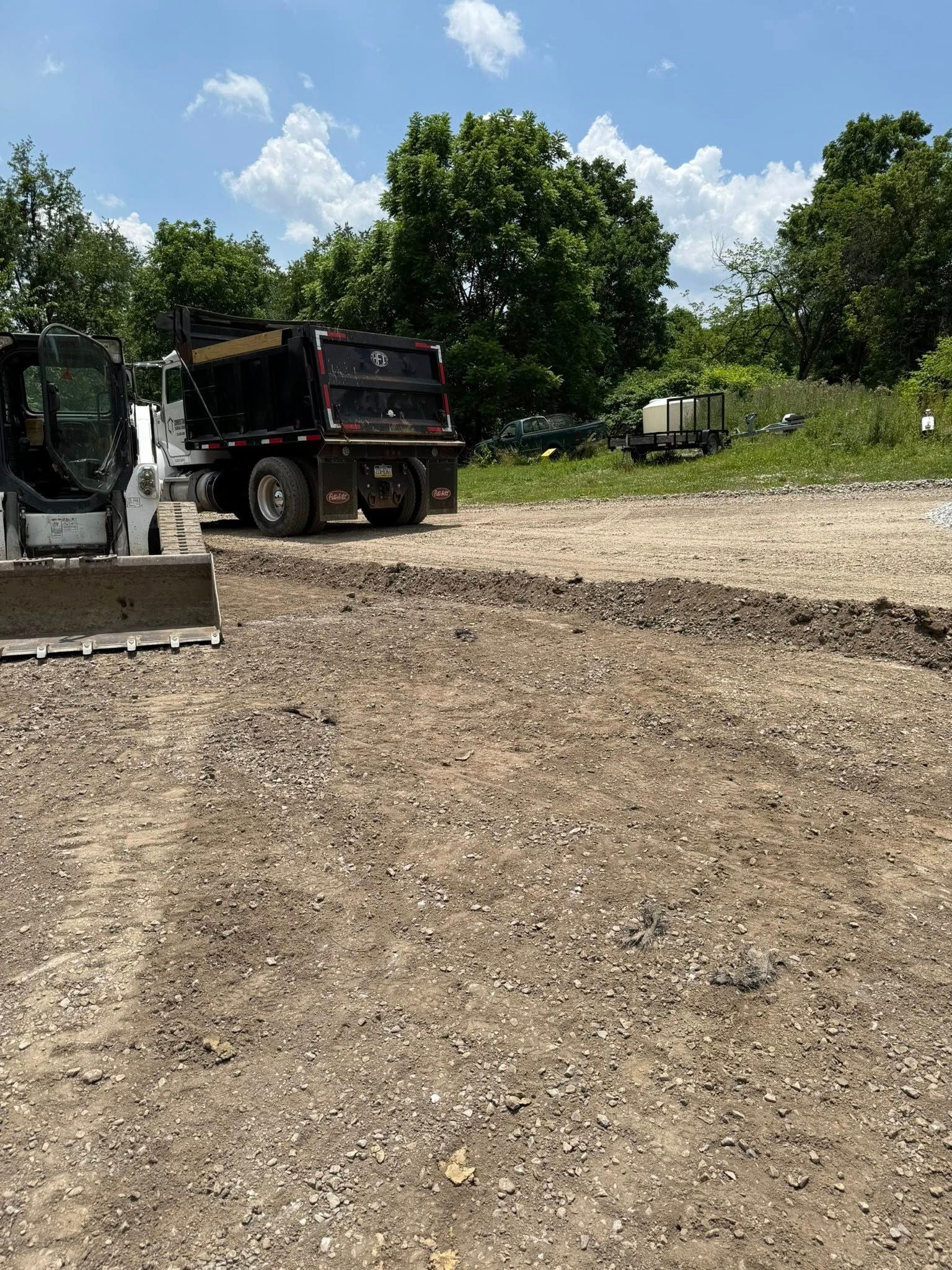 Construction site with a dump truck, a small bulldozer, and bare earth.  Trees and a blue sky are in the background.