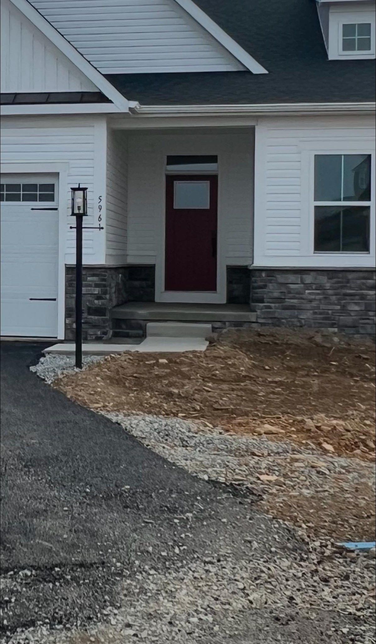 A white house with a red door. The entrance has dark stone accents and a lamp post sits in the driveway.