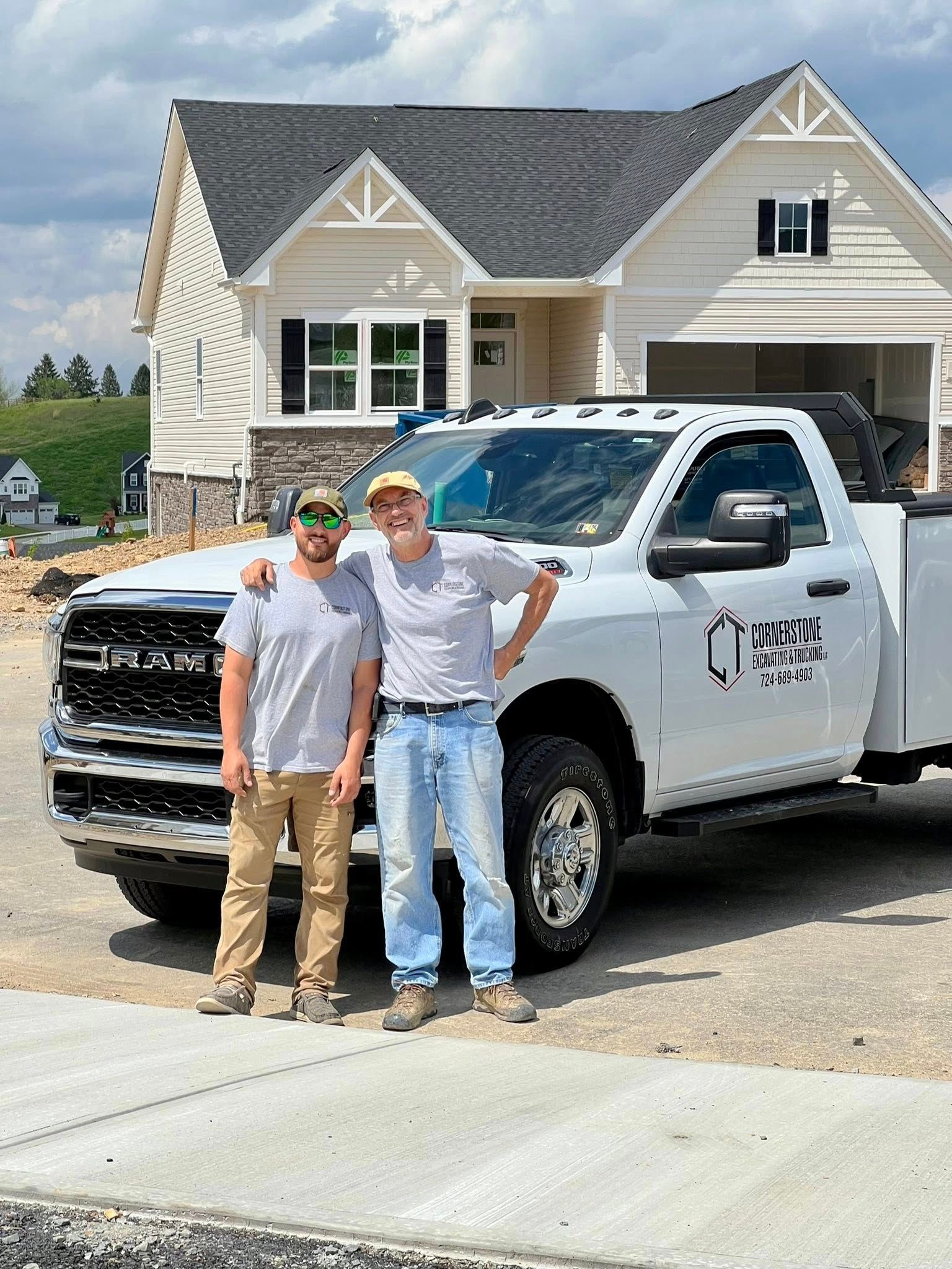 Two men standing in front of a white pickup truck and a newly built house. One man has his arm around the other.