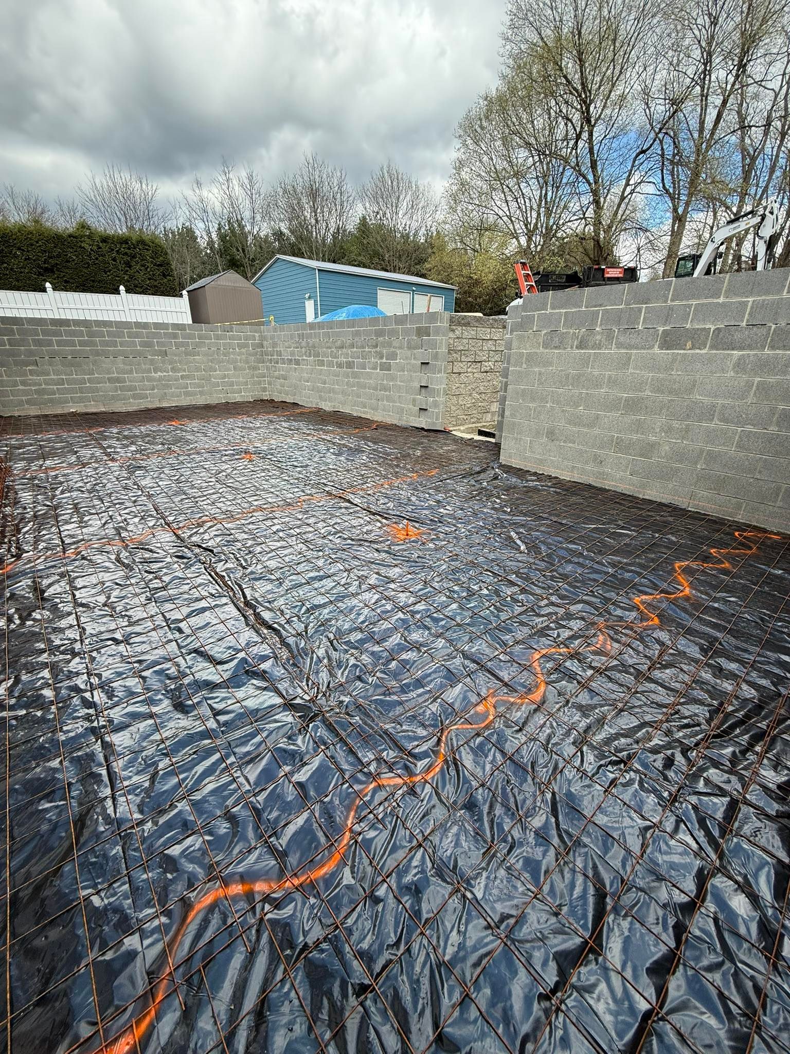 Black tarp covers a construction site, with concrete retaining walls in the background and a cloudy sky overhead.