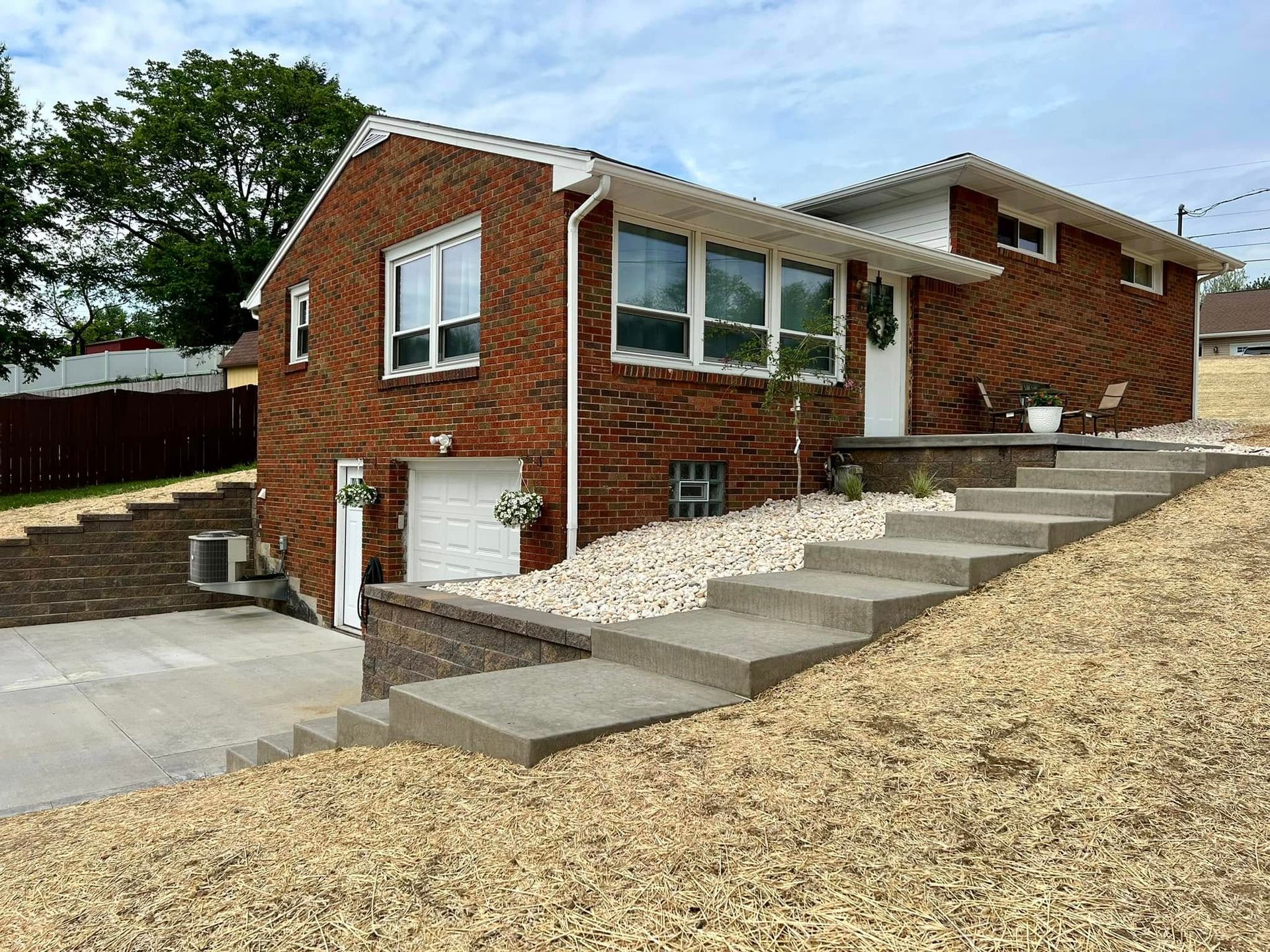 Brick house with a concrete staircase leading to the front door. The house sits on a sloped yard.
