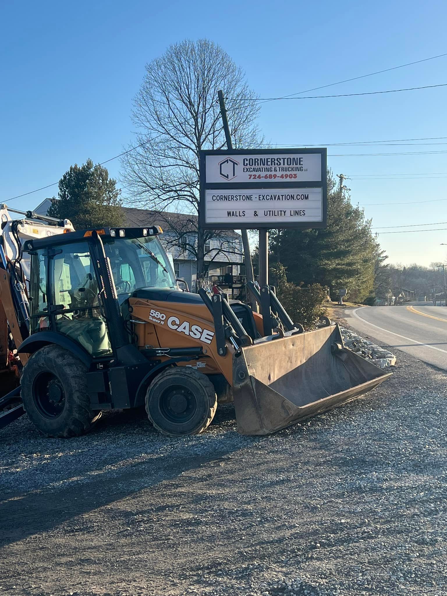 A Case backhoe parked on gravel next to a sign for a business, on a sunny day.