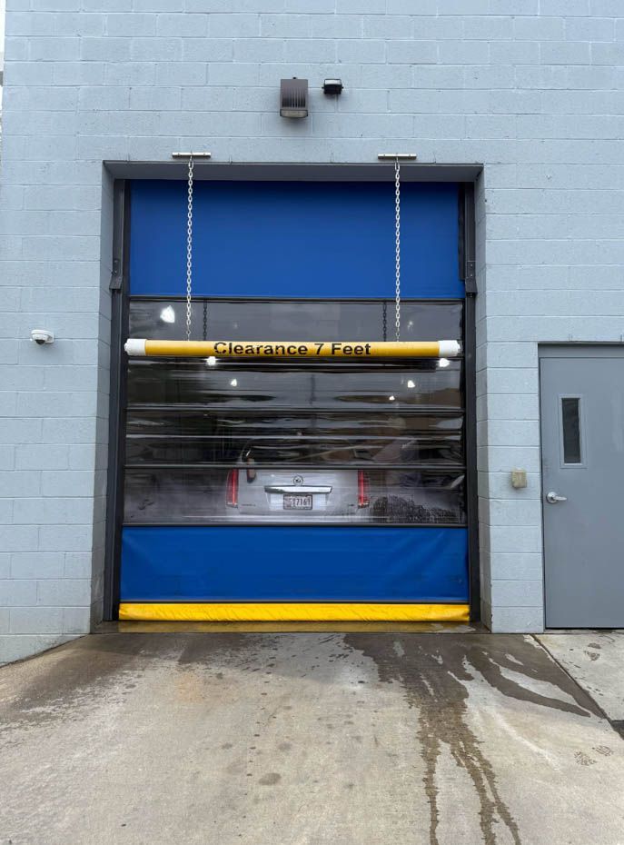 Blue and clear rolling door with yellow accents on a building with a clearance bar.