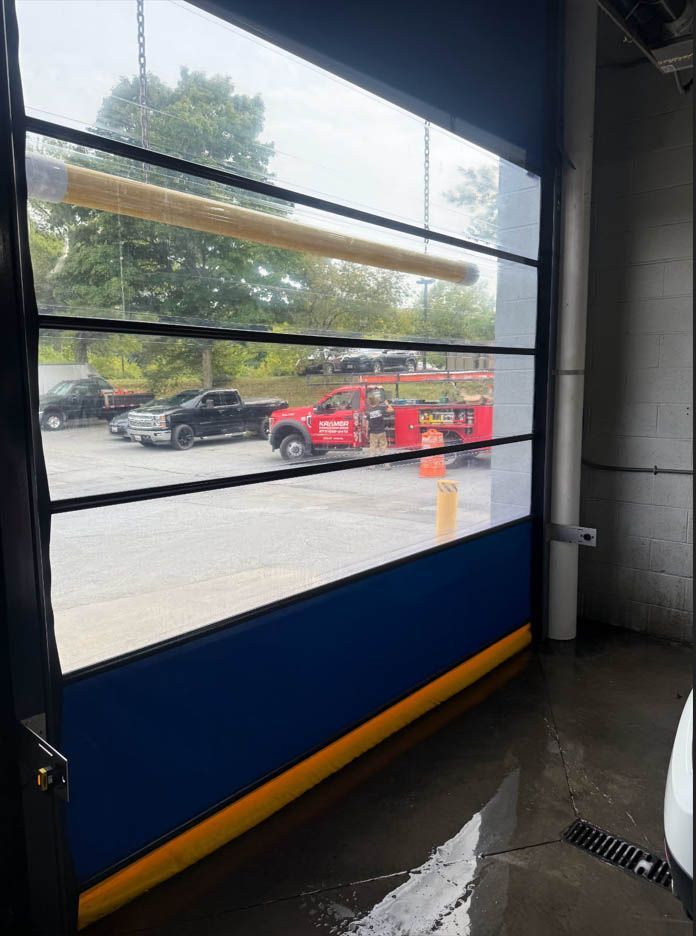 Blue and yellow industrial roll-up door open, revealing vehicles outside.