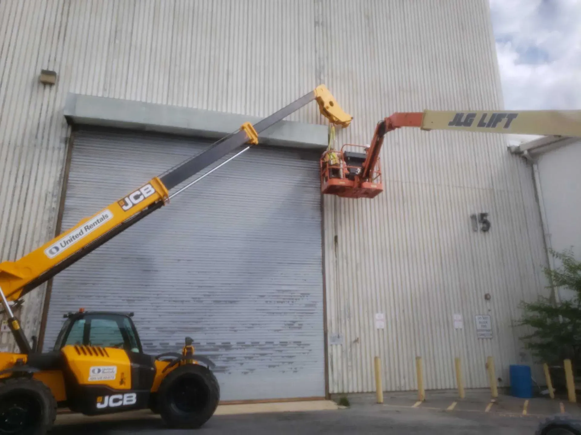 Two yellow lifts working on the facade of a warehouse building, one with a lift bucket.