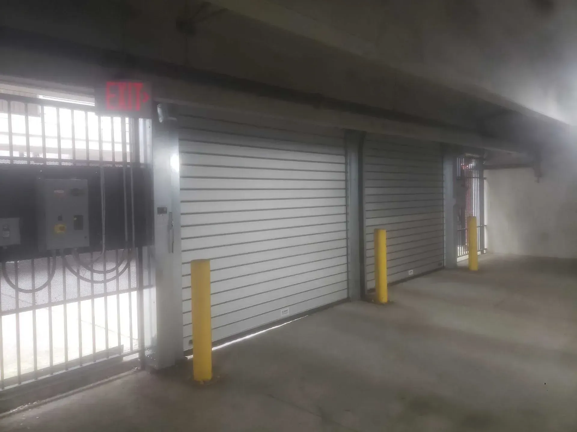 Rolling garage doors, metal gate, yellow safety poles in a parking structure.