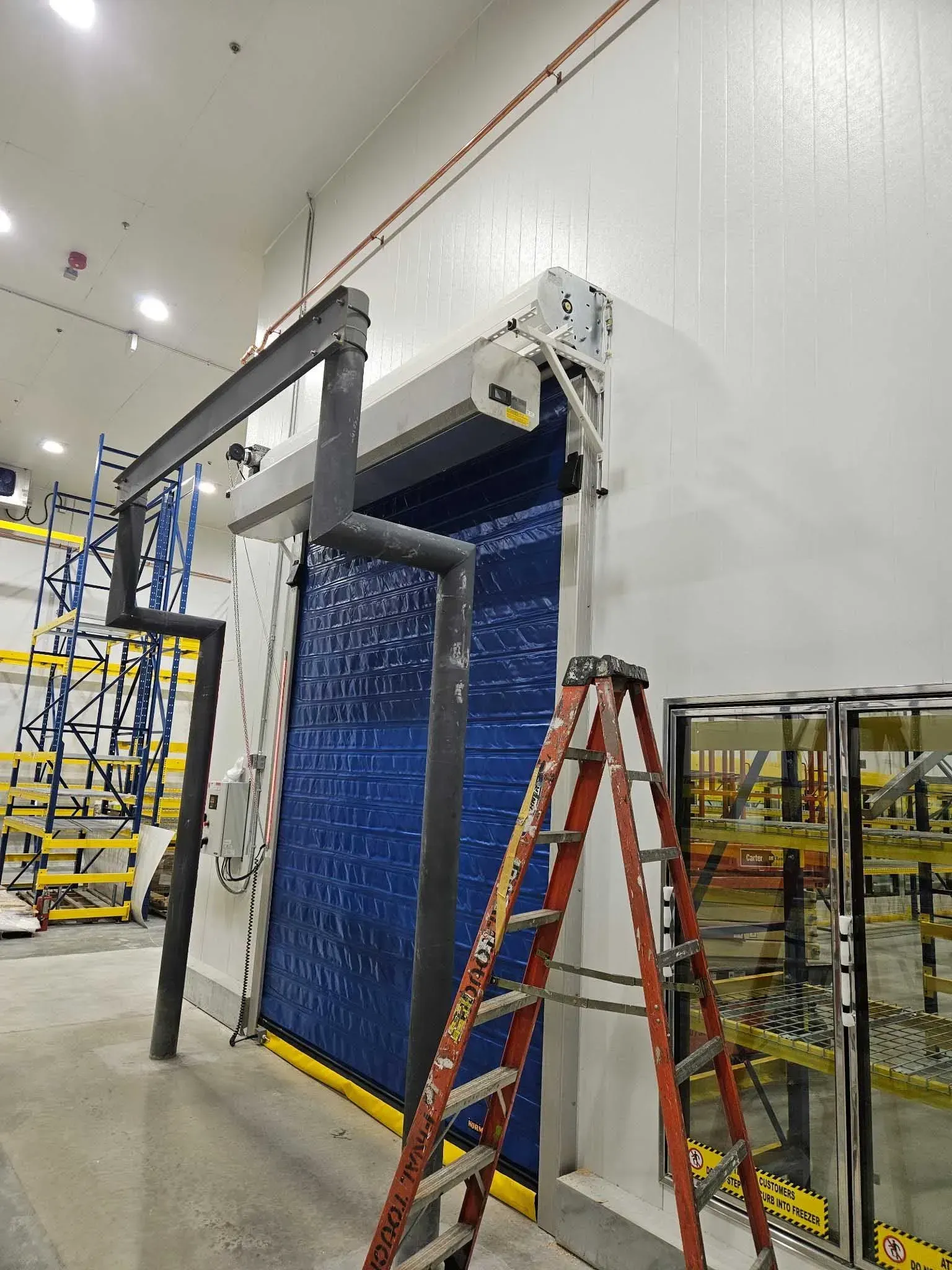Blue industrial door with black pipes, a red ladder, and warehouse shelving.