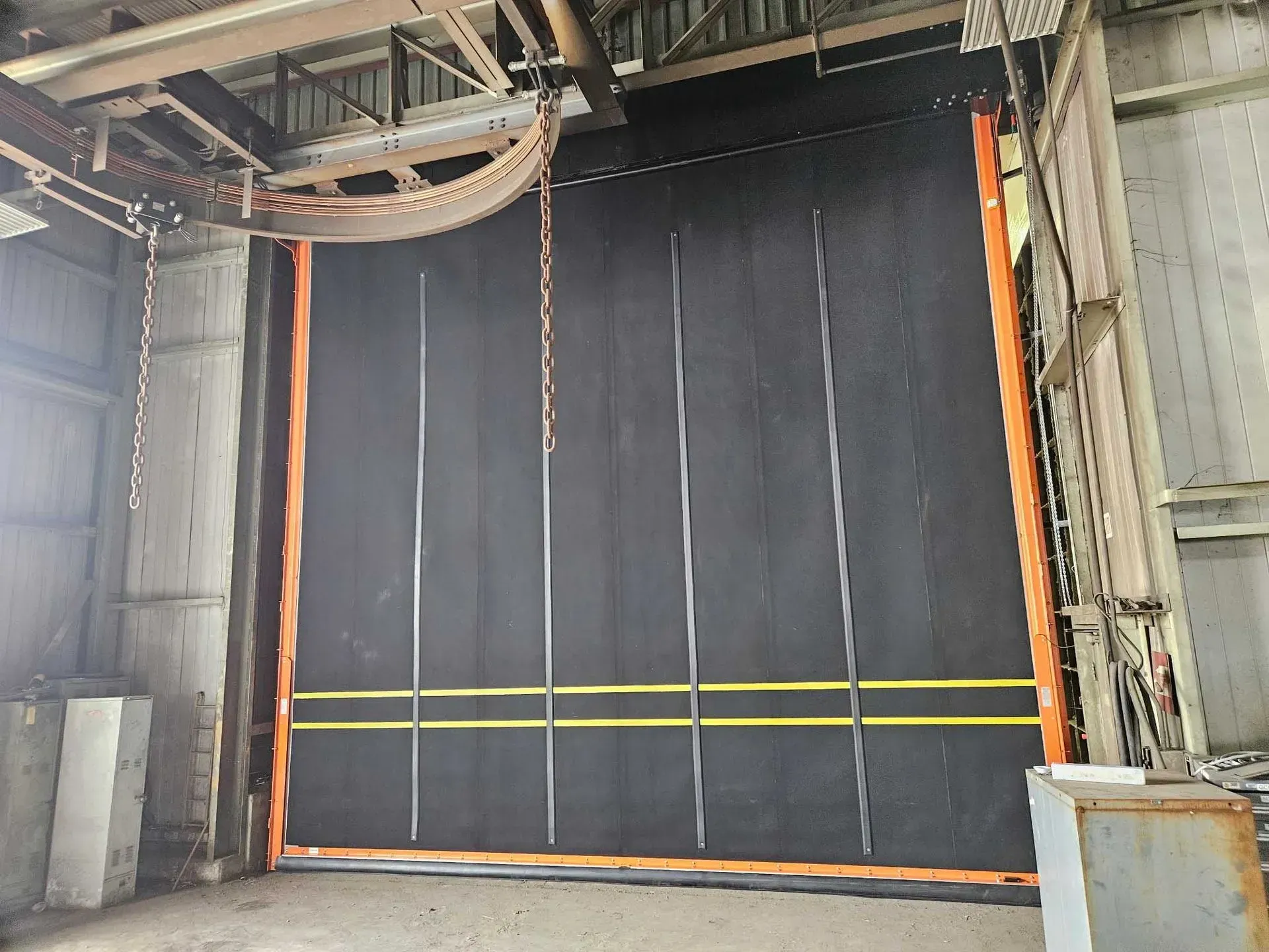 Black industrial roll-up door with yellow stripes, in a warehouse setting.