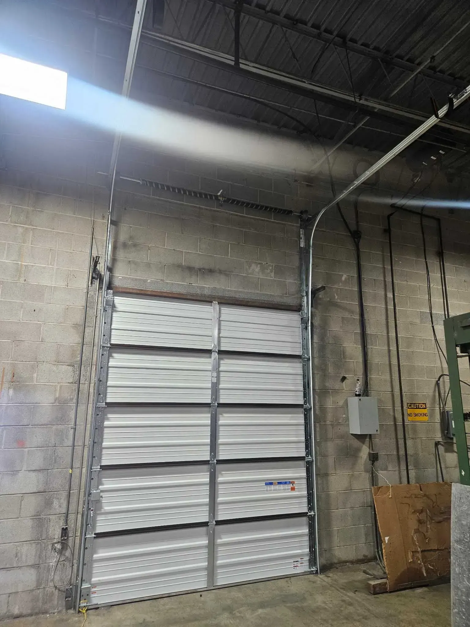 Interior view of an industrial garage door, made of white corrugated metal, within a brick warehouse.