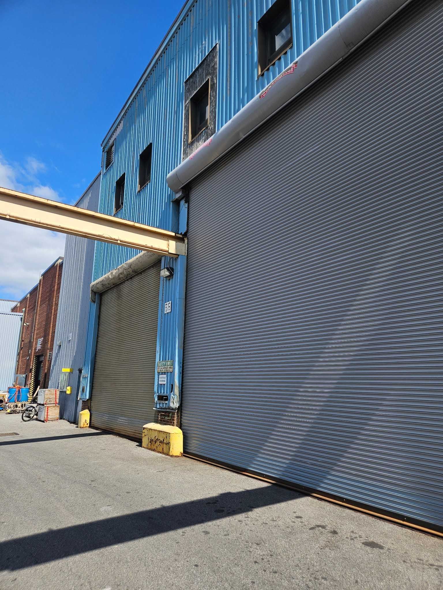Blue industrial building with large gray roll-up doors. A yellow metal walkway extends from the building.
