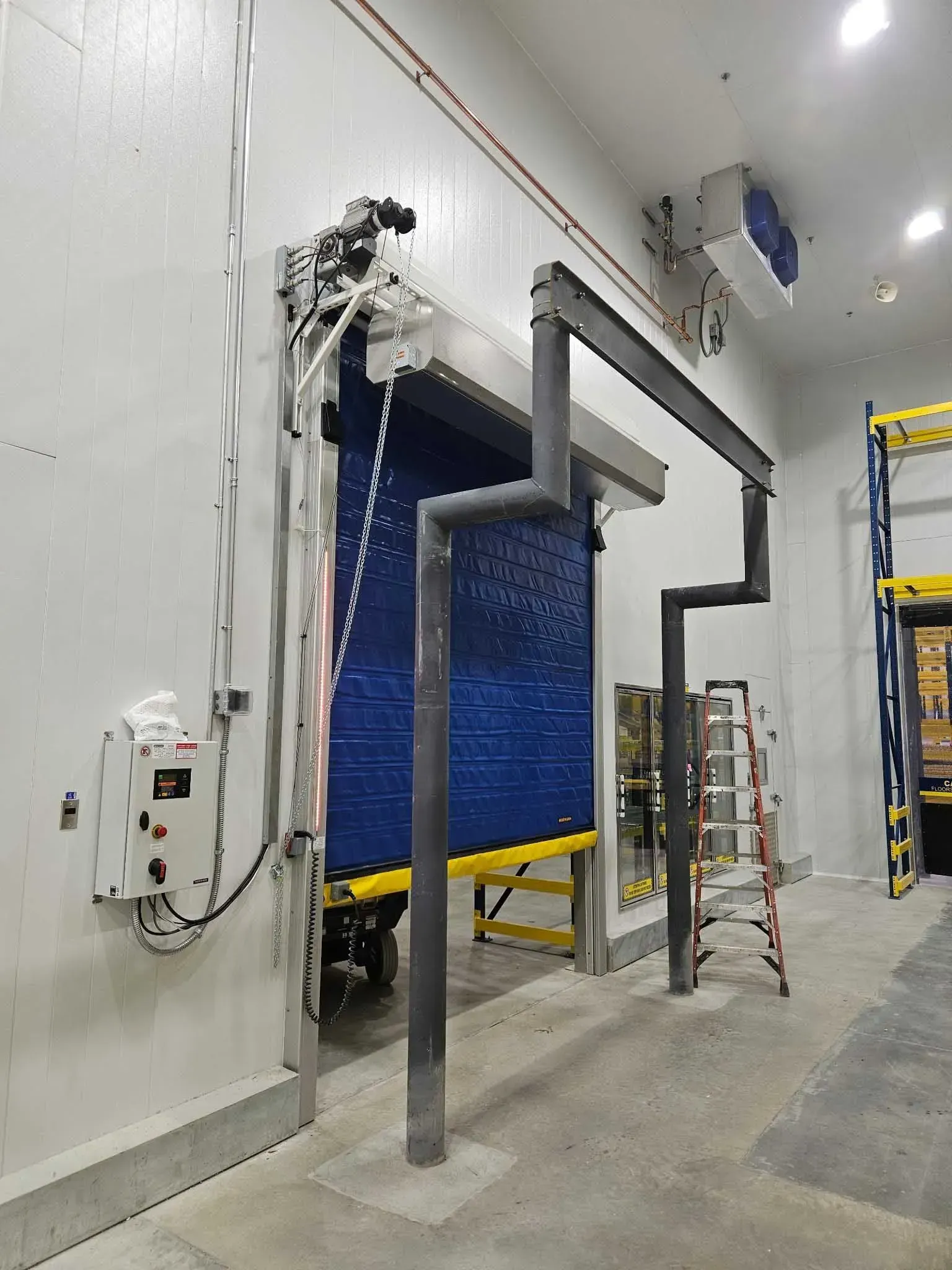 Blue insulated door in a walk-in cooler. Grey piping and control box are visible. White and gray walls.