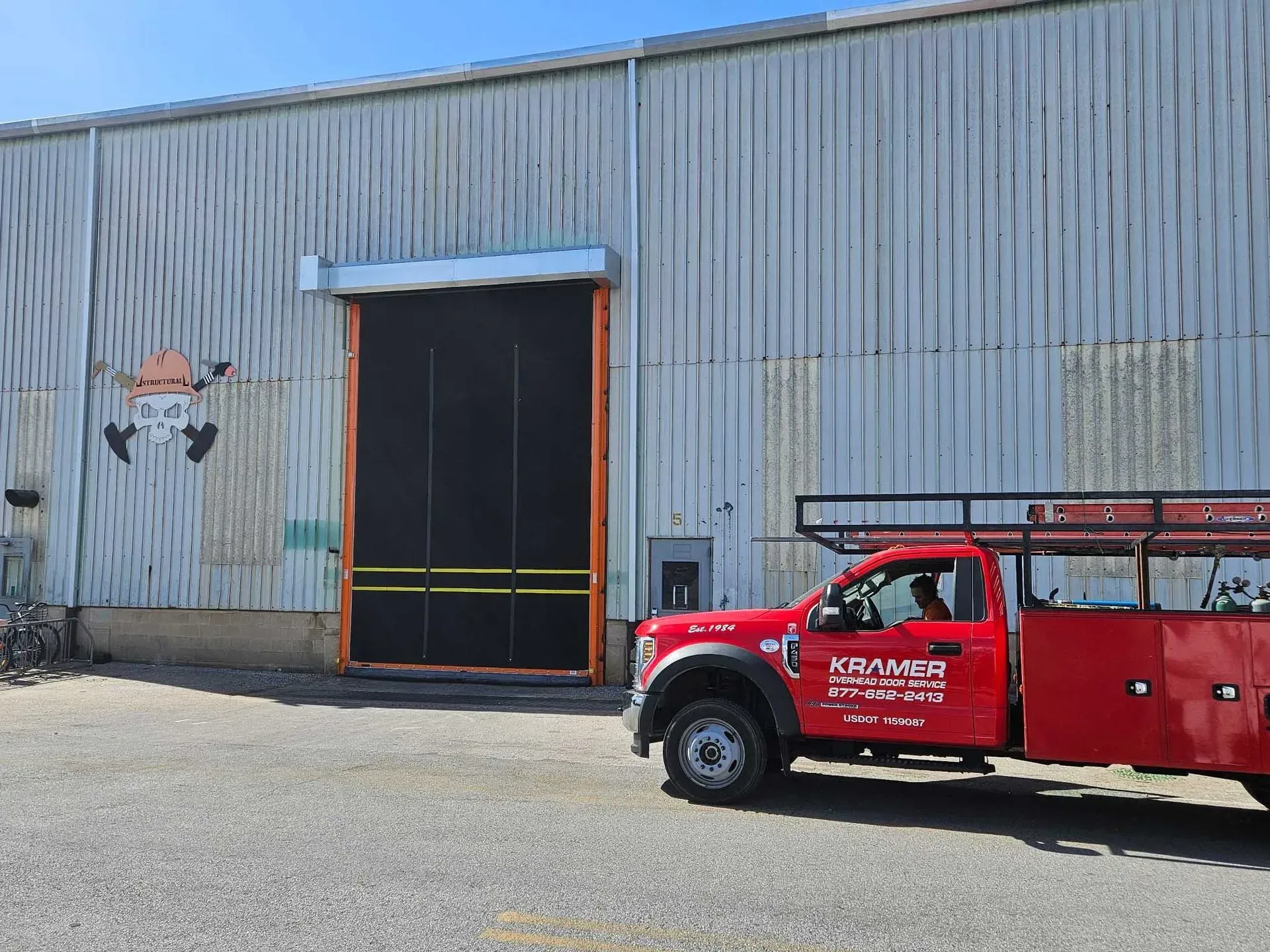 Red truck parked in front of warehouse with open door. Orange trim, black screen. Cartoon fox on wall.