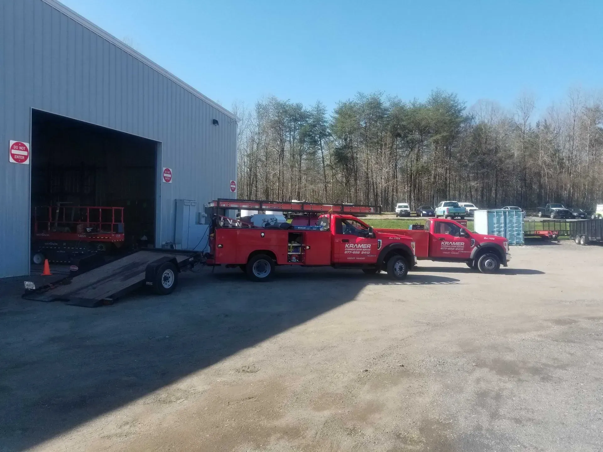 Red service trucks parked outside a large building with a trailer. Sunny day.