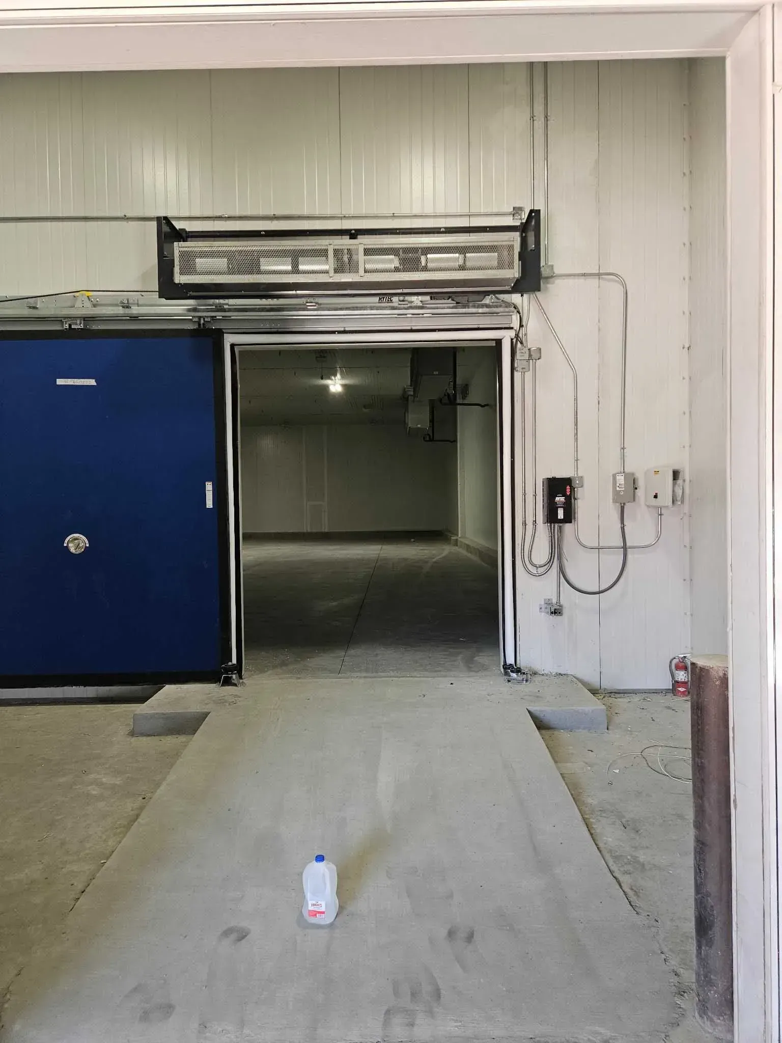 Blue sliding door leads to an empty white interior. Concrete ramp, bottle on floor.